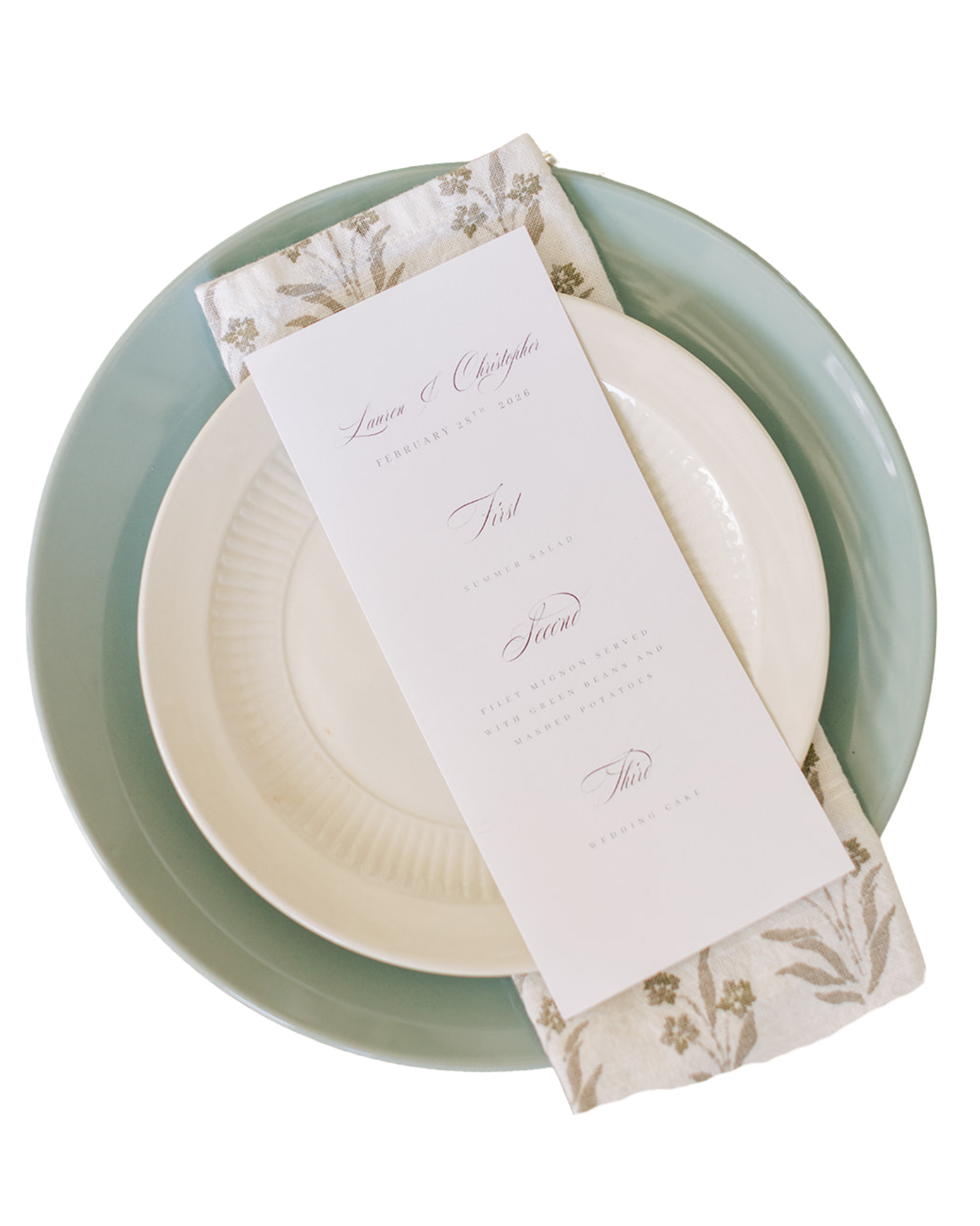 A white paper with elegant script announcing a wedding date and names, placed on white and green china plates on a tray with a cloth napkin.