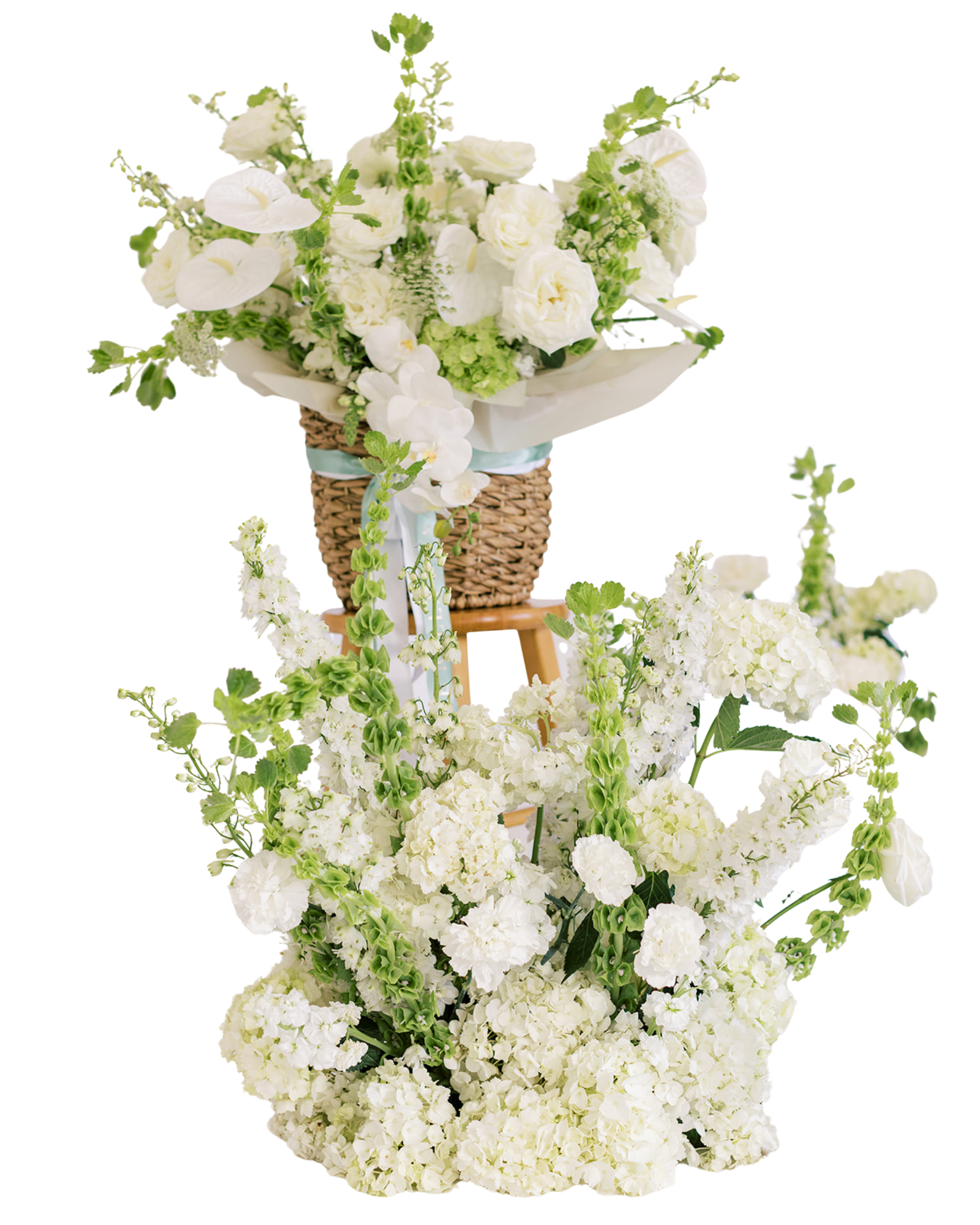 A large floral arrangement in a wicker basket with white and green flowers, including roses and orchids, on a small stand with greenery cascading down.