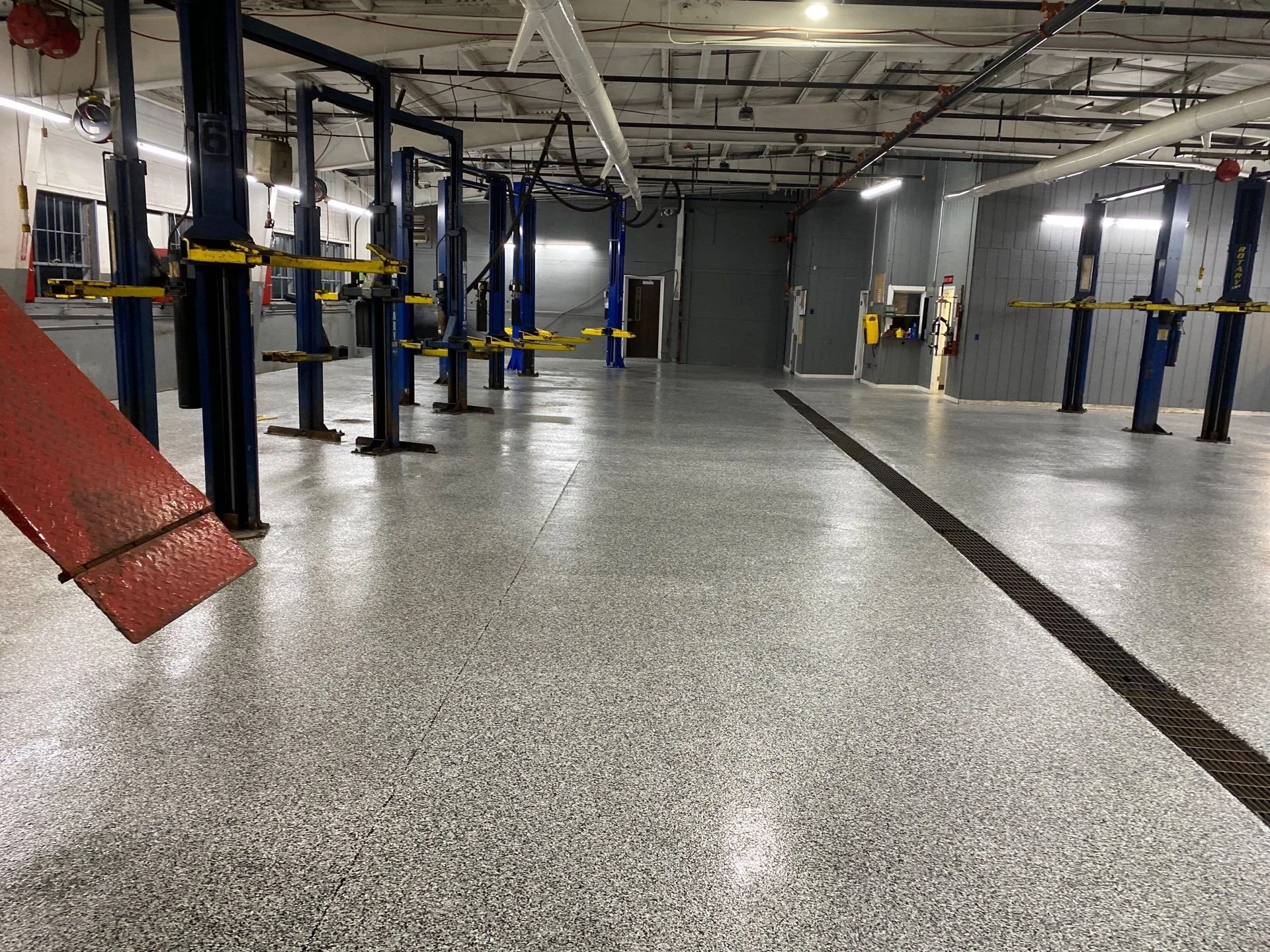 Empty car repair shop with vehicle lifts, a red ramp, and industrial ceiling pipes.
