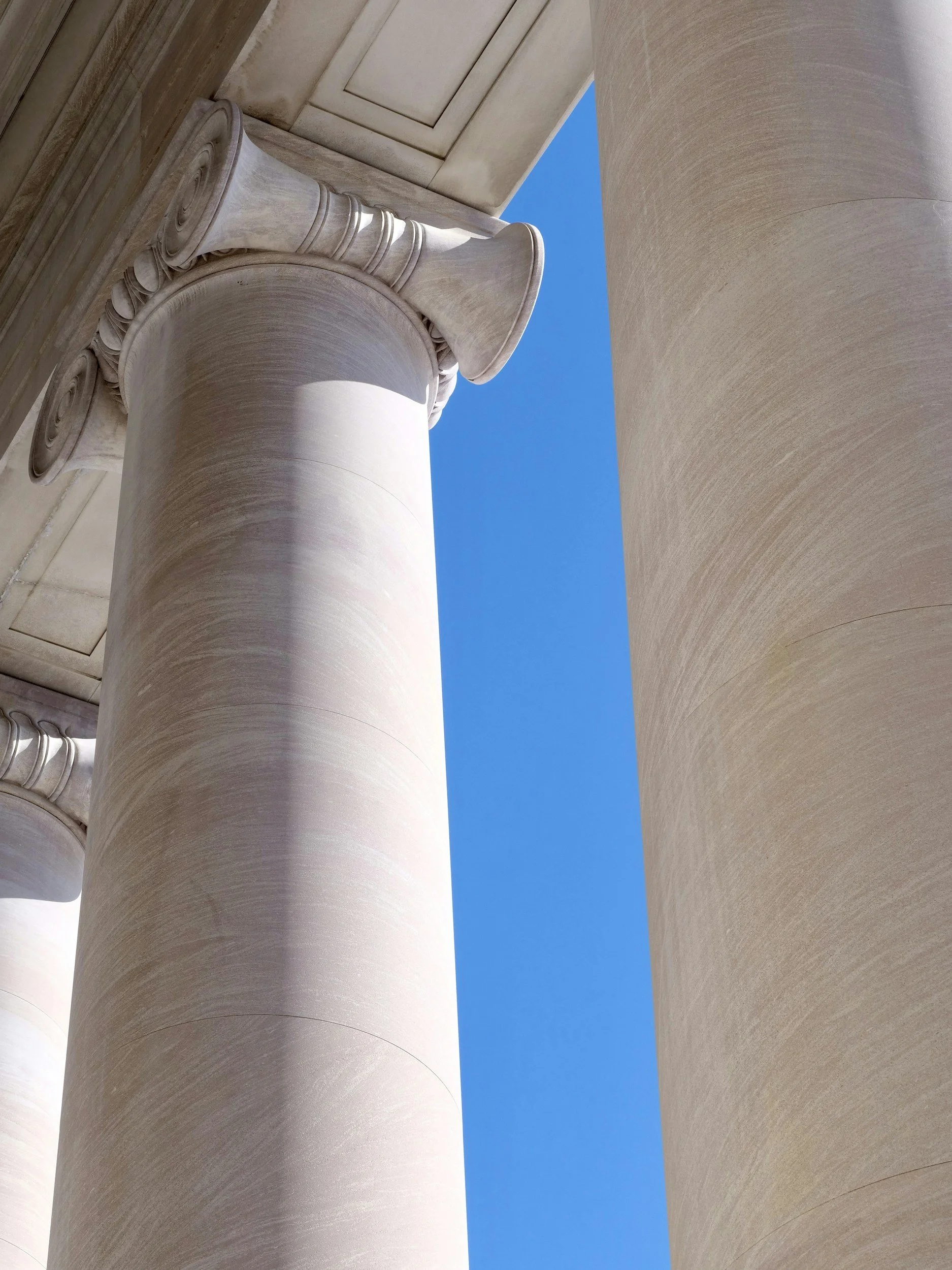 Close-up of large stone columns with detailed architectural carvings against a bright blue sky.