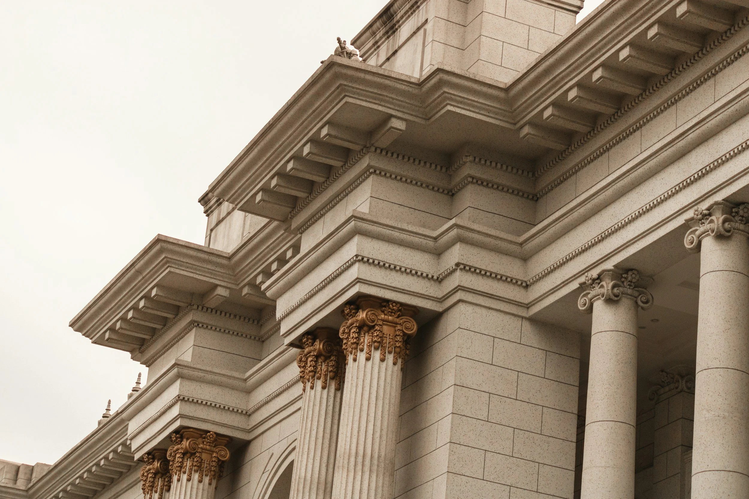 Close-up of a neoclassical building with detailed columns and ornate cornices, showing a corner with a decorative arch and pilasters against an overcast sky.
