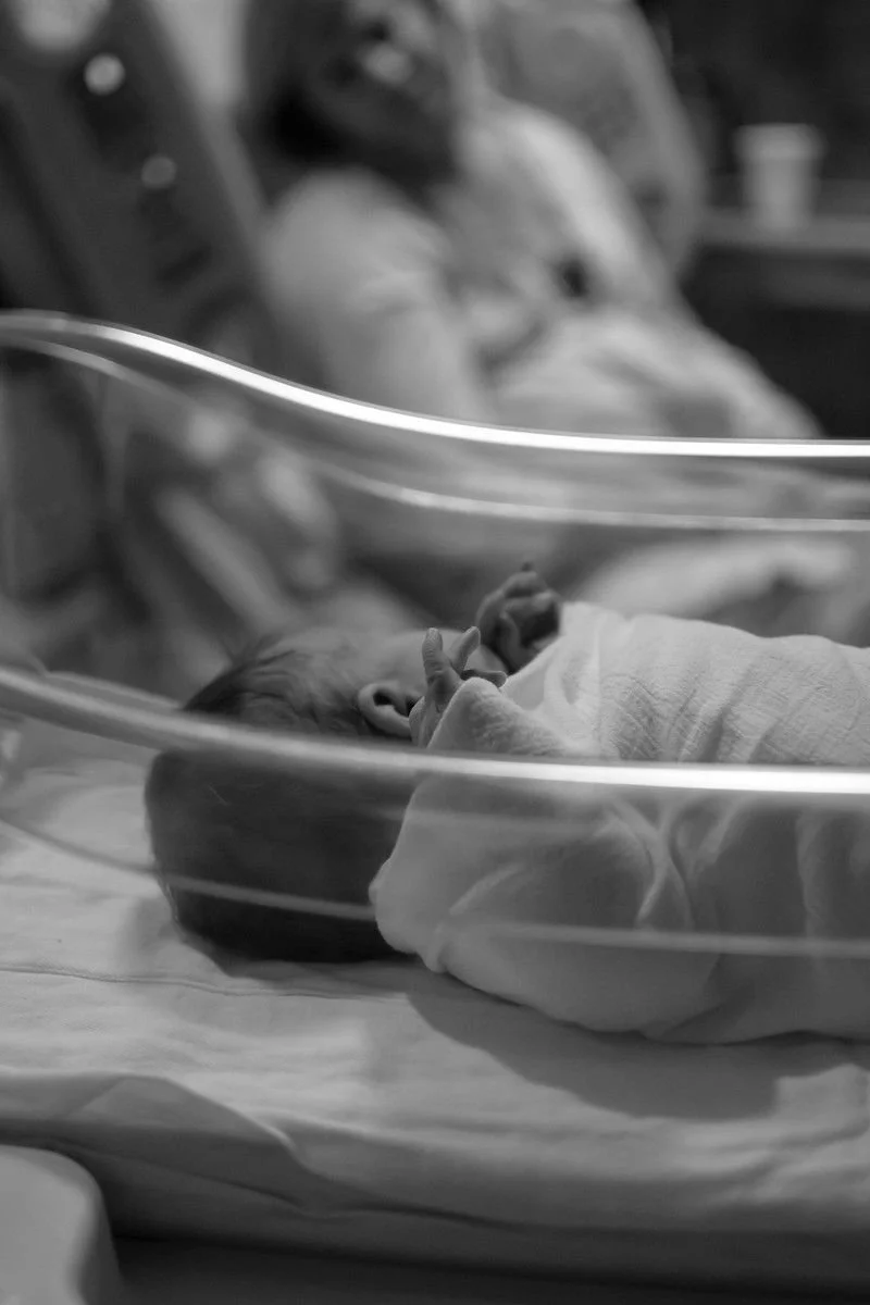 Newborn resting in an incubator with a parent lovingly nearby.