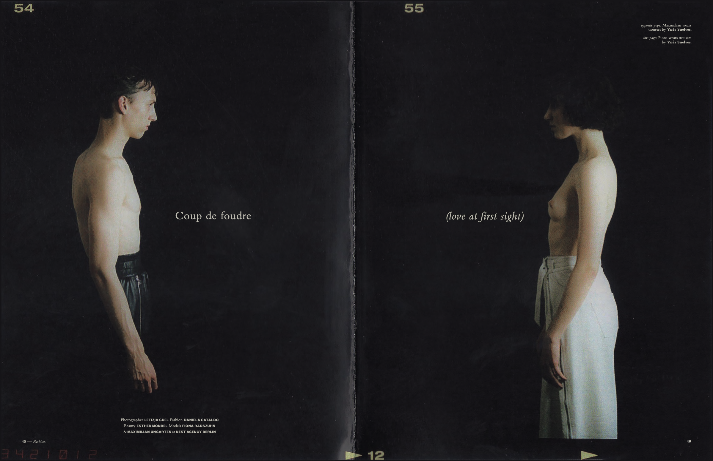 Two women stand in profile against a black background, one with short curly hair wearing beige trousers, and the other with short straight hair wearing black trousers. The left woman is labeled Fiona, and the right woman is labeled Ynes. The text indicates Ynes wears trousers, and Fiona wears trousers. The image is a fashion photograph with credits to the photographers and stylist at the bottom.