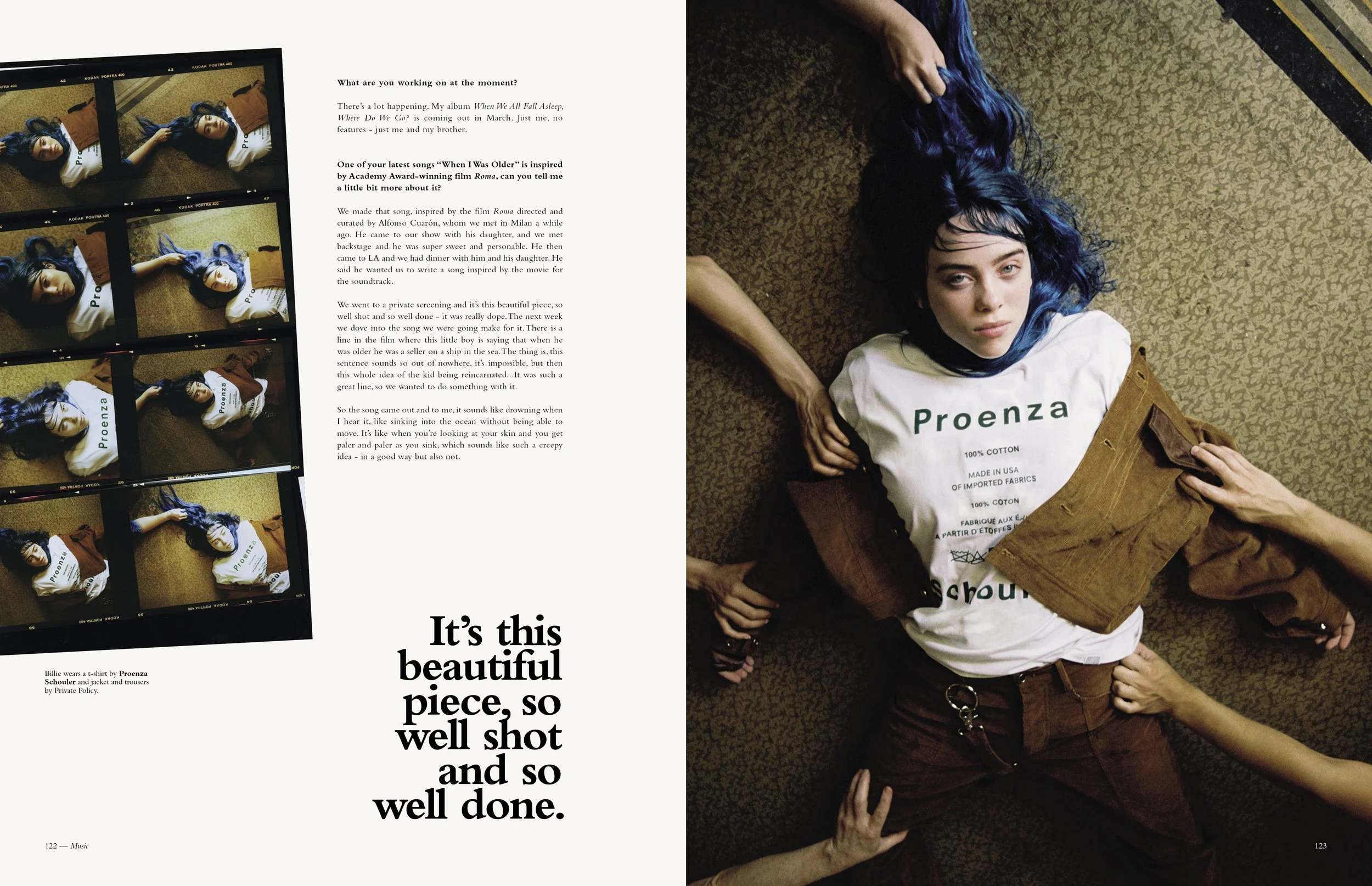A magazine page displaying a photograph of a young woman with long blue hair, lying on a textured brown carpet. She wears a white t-shirt with "Proenza" printed on it and brown pants. Multiple hands are reaching towards her from different directions, some touching her hair and arm. The opposite page contains black text and additional images of her lying on the carpet with her eyes closed.
