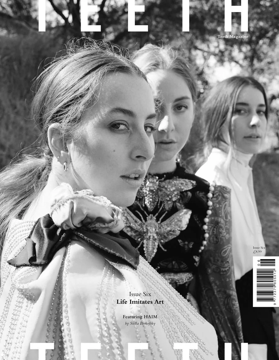 Black-and-white magazine cover featuring three women posing outdoors, with the woman in forefront looking directly at the camera, wearing a fancy embroidered blouse with a neck ruffle and ribbon detail; the other two women behind her also looking at 