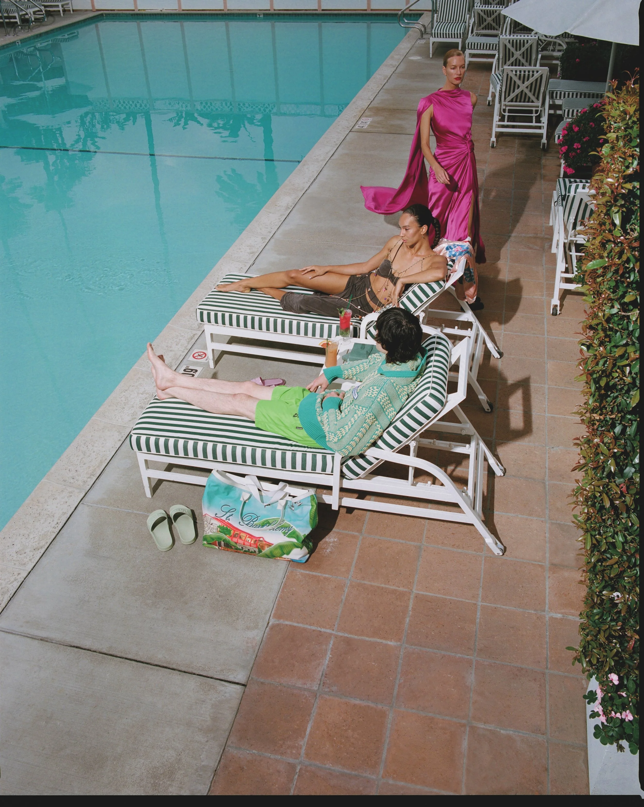People relaxing poolside with lounge chairs, an empty swimming pool, and colorful flowers on the side.