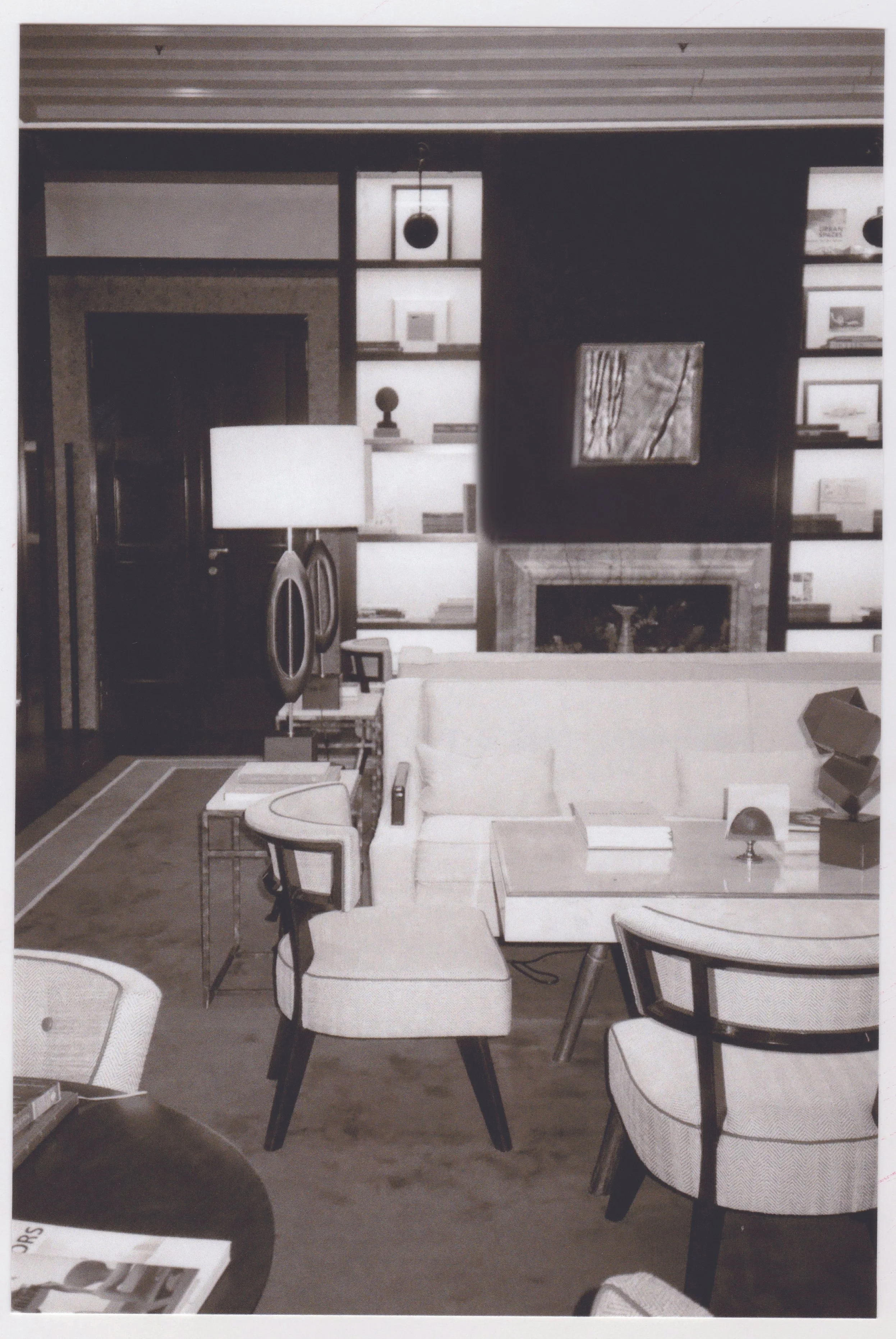 A modern living room with a fireplace, bookshelf, and seating area including chairs and a white sofa, decorated with art and accessories.