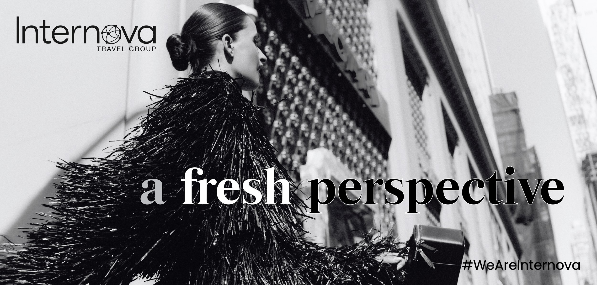 Black and white photograph of a woman with hair in a bun, wearing a textured, shiny black coat, standing in a store aisle with shelves of shoe boxes in the background. The image includes text that reads "Internova Travel Group" in the top left corner