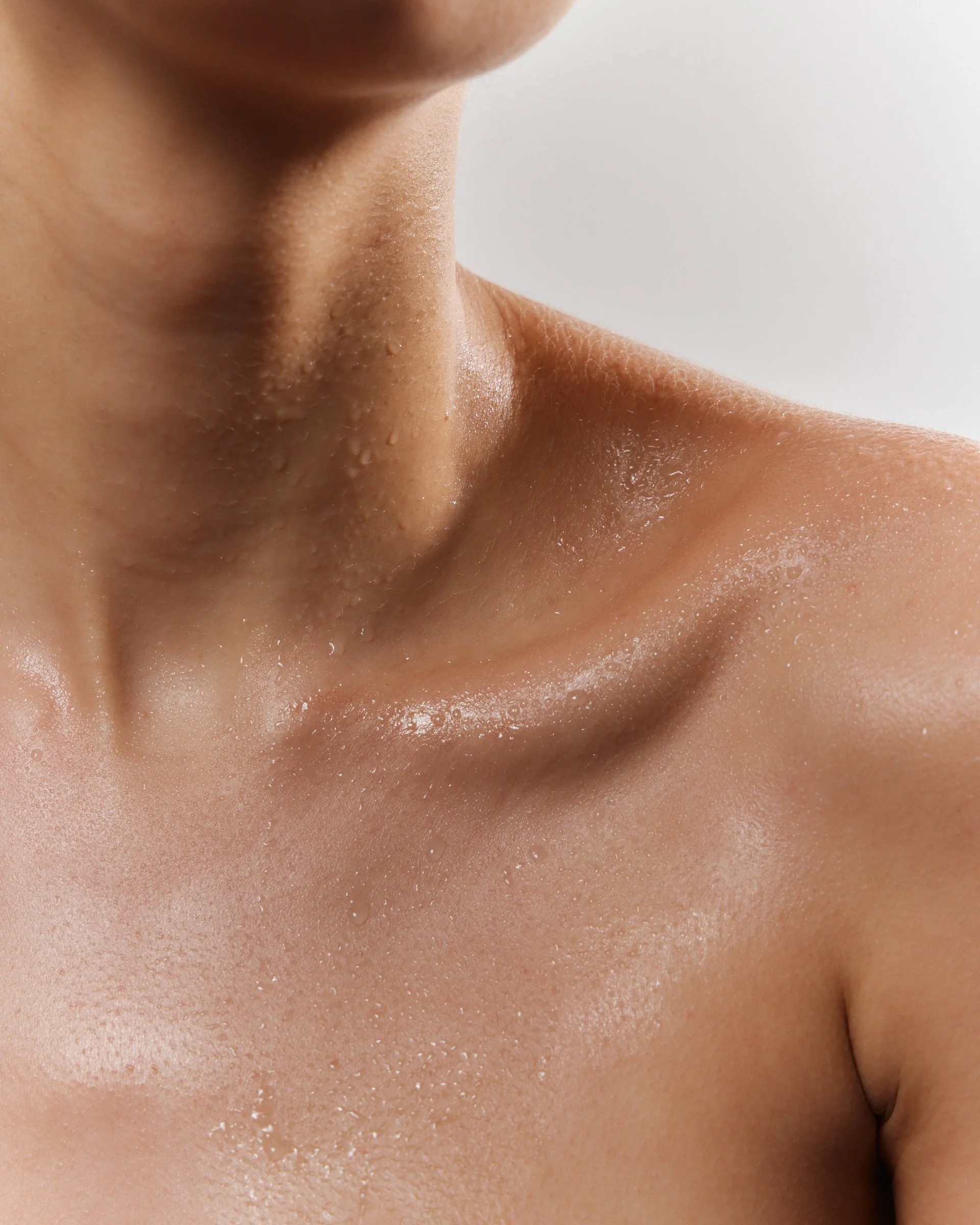 Close-up of a person's neck and shoulder with water droplets on their skin.
