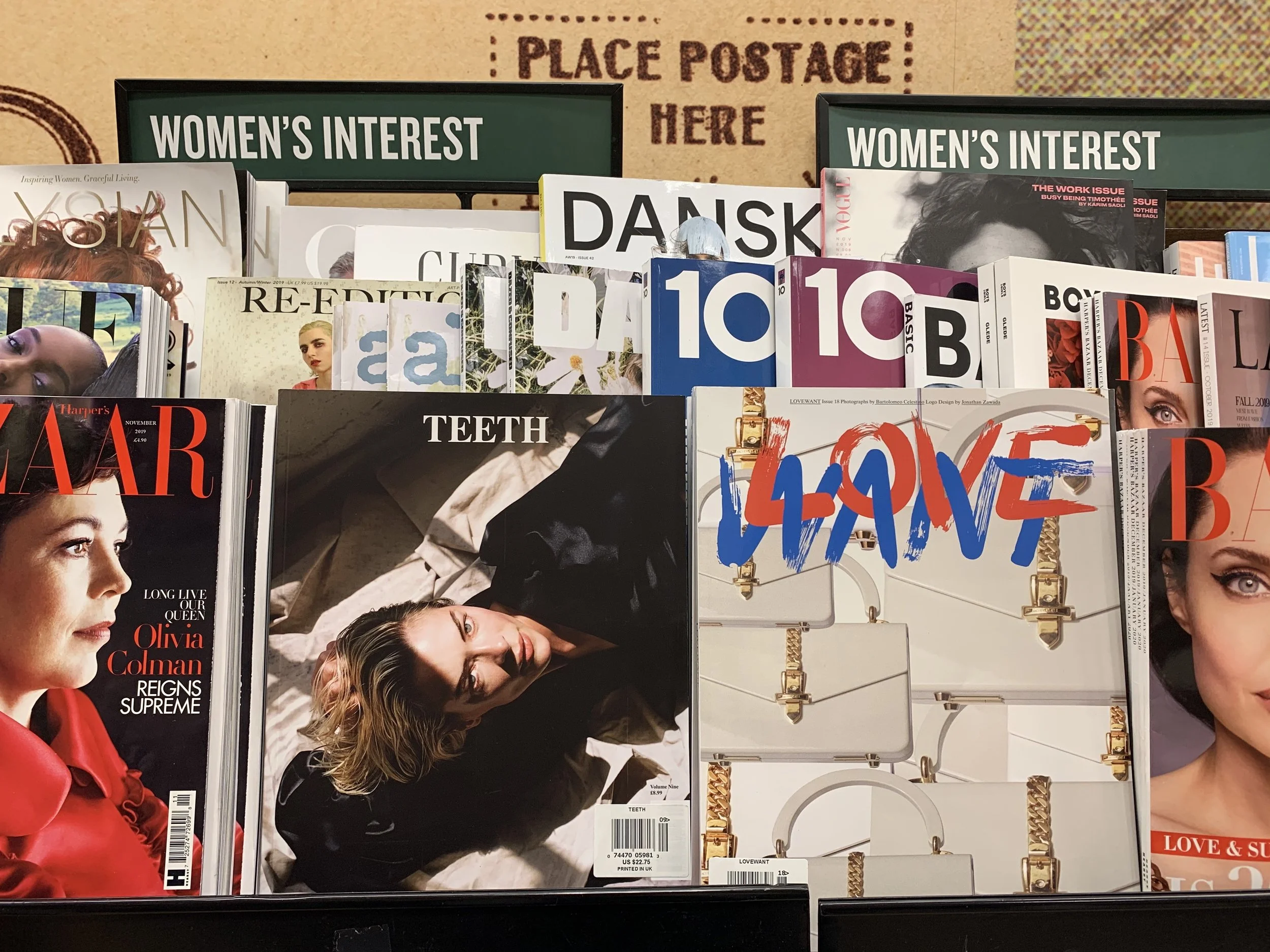 Magazine display on a shelf labeled 'Women's Interest' featuring various fashion and lifestyle magazines, including covers with women and text about fashion, beauty, and culture.