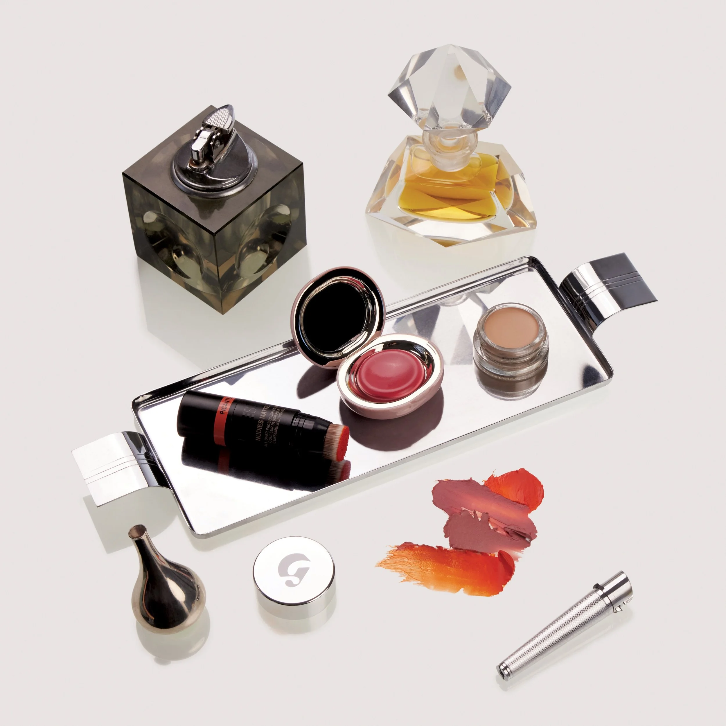 Various makeup and cosmetic products including lipstick, eyeshadow, gloss, brushes, and perfume bottles arranged on a white surface.