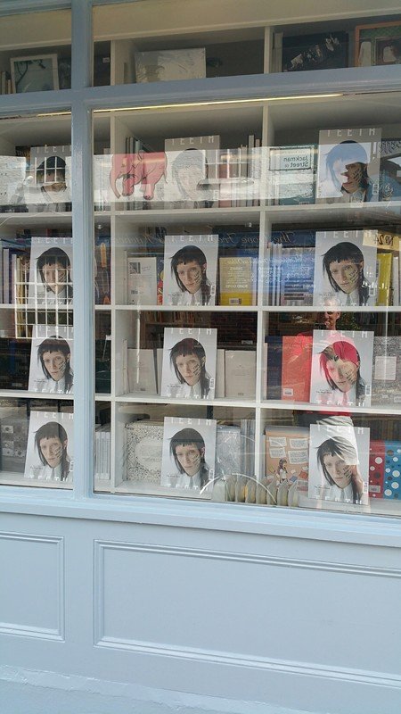 Bookstore window display with magazine covers featuring women's faces and a few books.