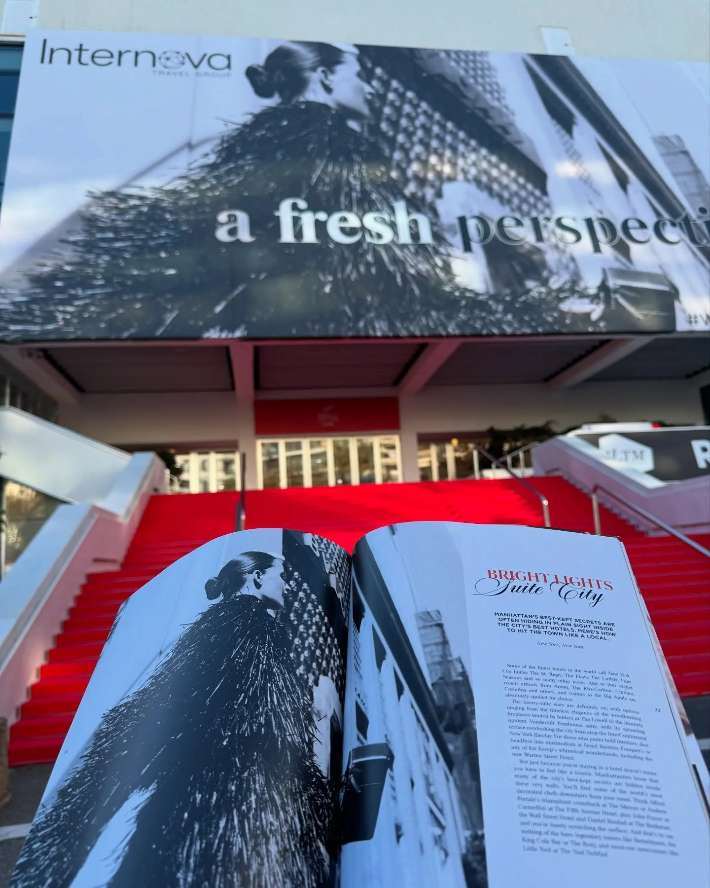 A magazine or brochure open to a page with the title "Bright Lights, Little City" featuring a black-and-white photo of a woman with a bun in her hair and feathered apparel. The background shows to a red staircase and an overpass or building structure