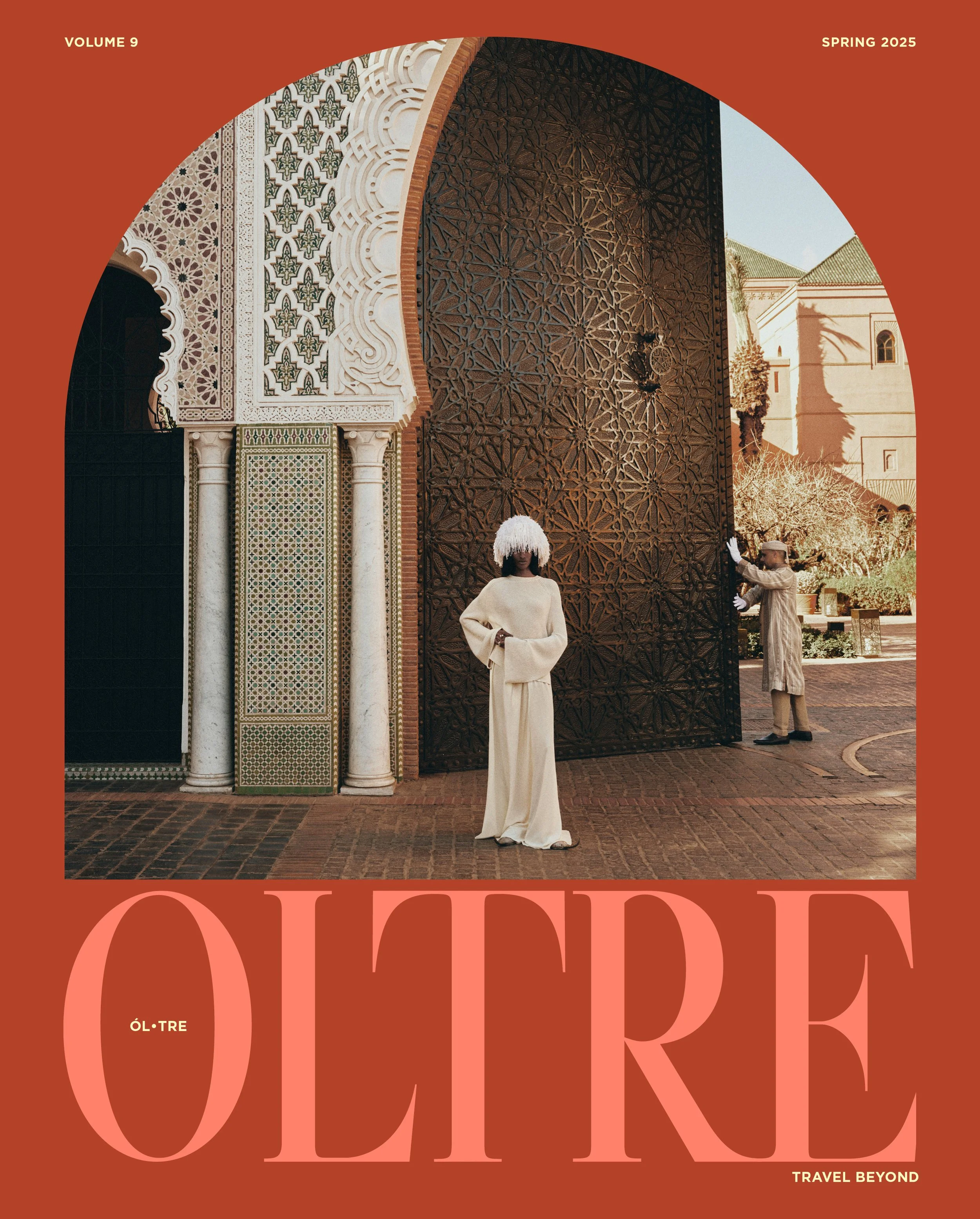 A woman in a white dress and a white headpiece stands in front of a large ornate wooden door with intricate geometric designs. Two other people are visible: a man in traditional attire and a woman in the background. The architectural style suggests a Middle Eastern or Moroccan setting, with decorative arches and patterned tilework.