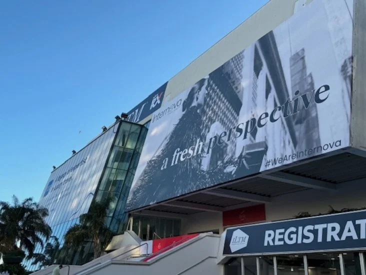 Exterior of a modern building with large glass windows and a prominent billboard displaying urban skyline images and the text 'a fresh perspective'.