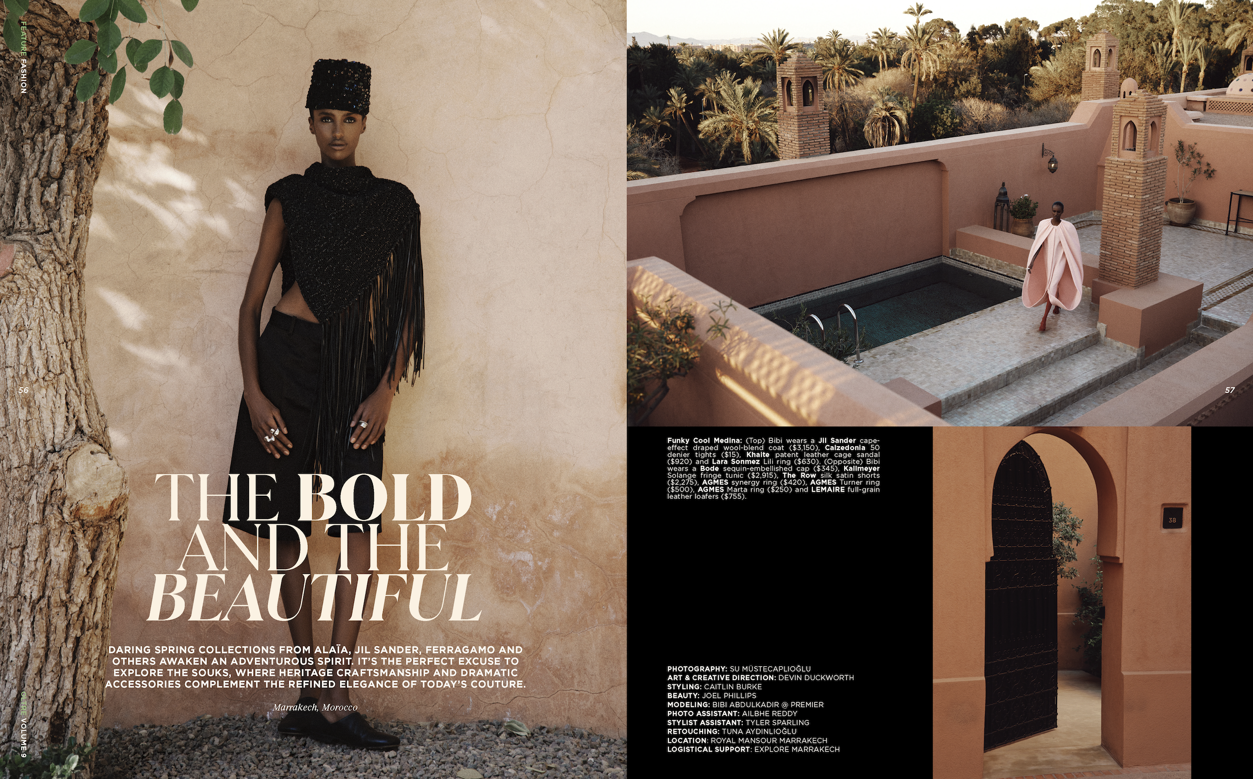 A woman dressed in black with a fringe cape, standing next to a tree in a desert-like setting with a pink wall and a pool, adjacent to a beige wall in a Moroccan style courtyard, with palm trees in the background.