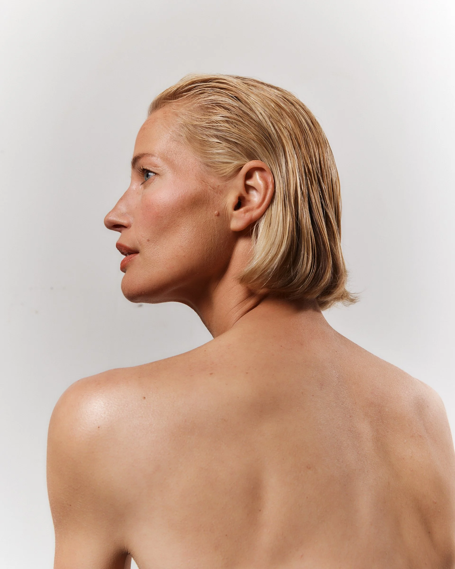 Close-up side profile of a woman with wet blonde hair and smooth skin, against a plain white background.