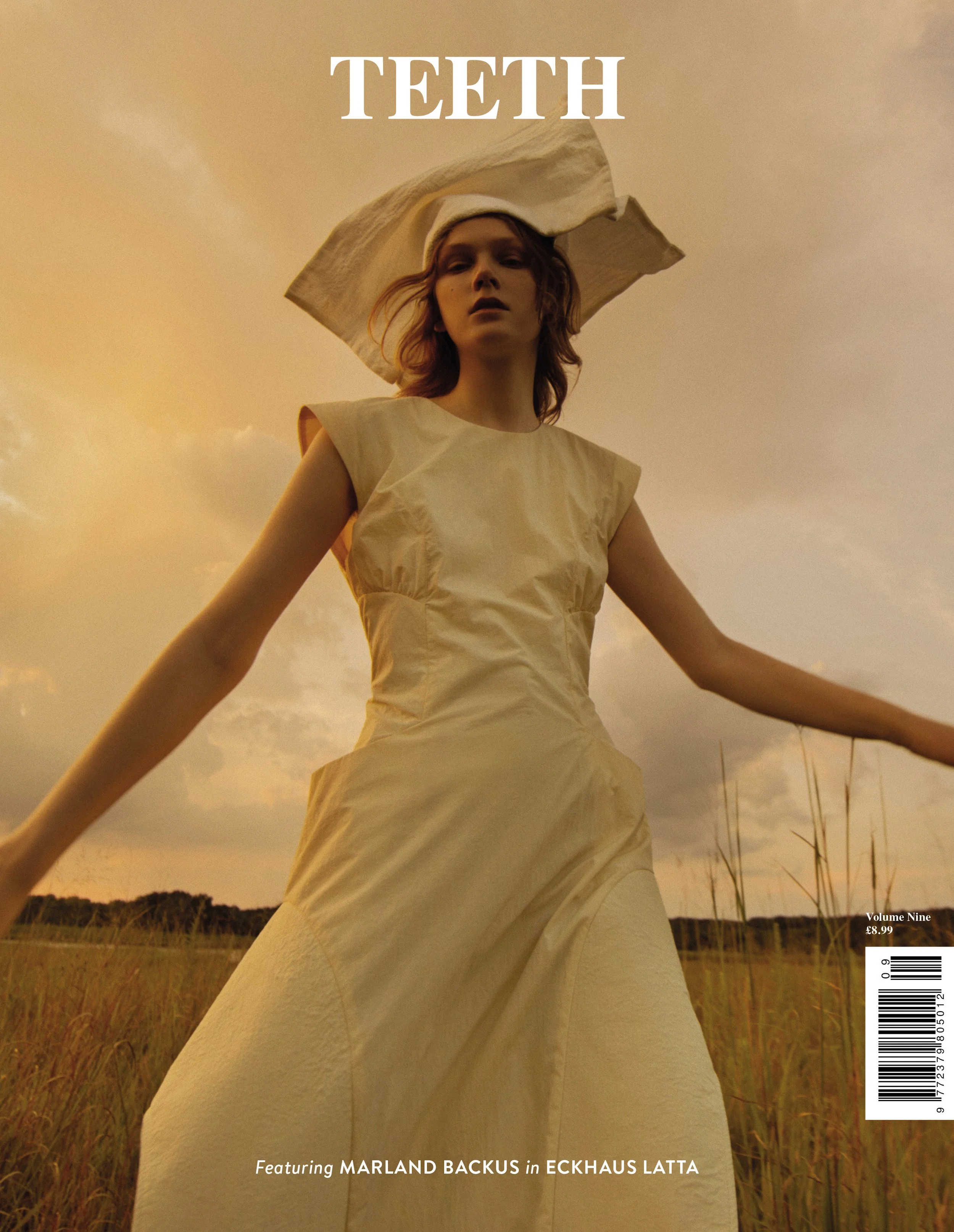 A woman wearing a cream-colored dress and large hat with a bill, standing in a field of tall grass at sunset. The sky is warm and cloudy. The magazine cover features the title "TEETH" at the top, with additional text at the bottom indicating a featur