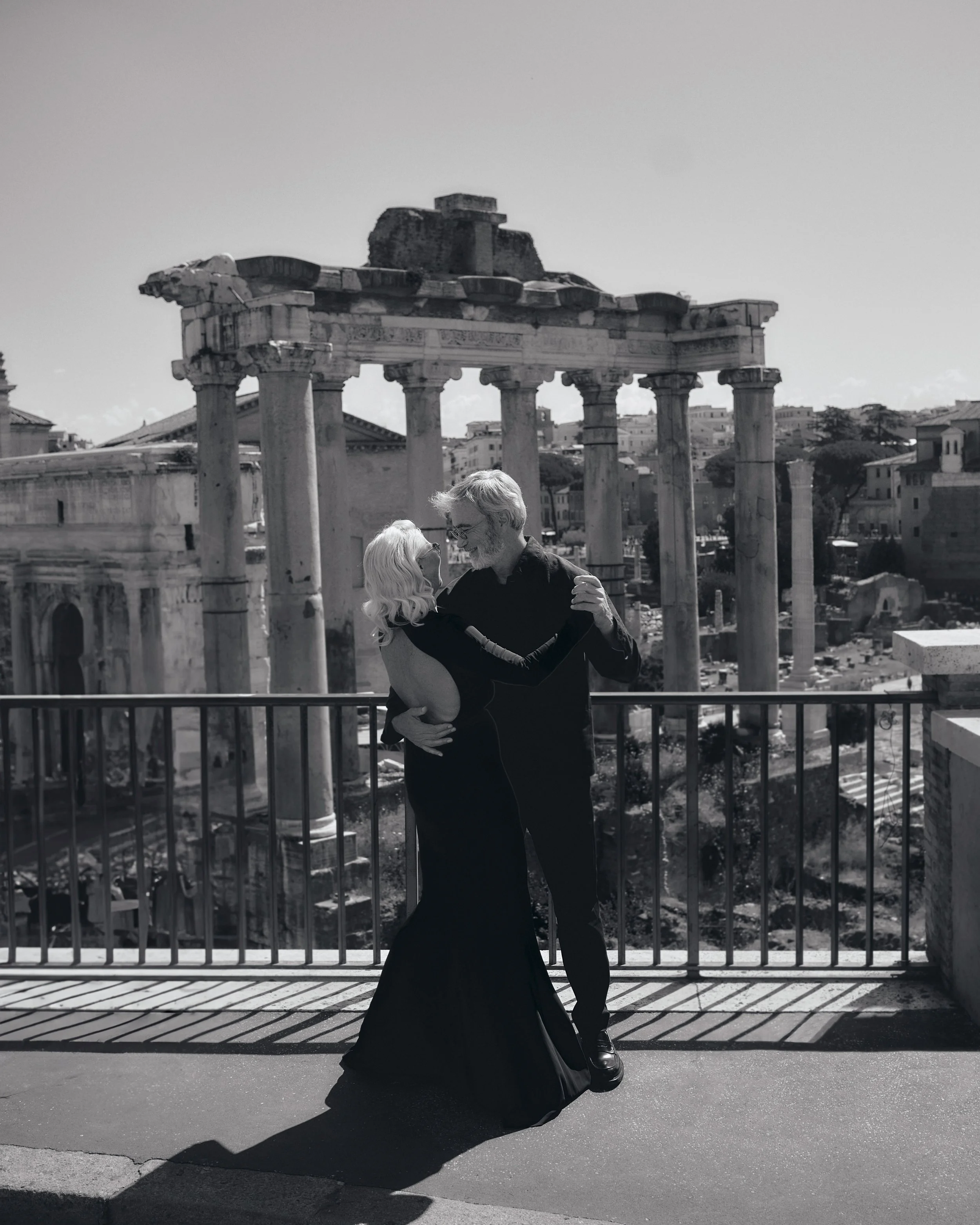 A couple dancing outdoors in front of ancient ruins with columns, under a clear sky.