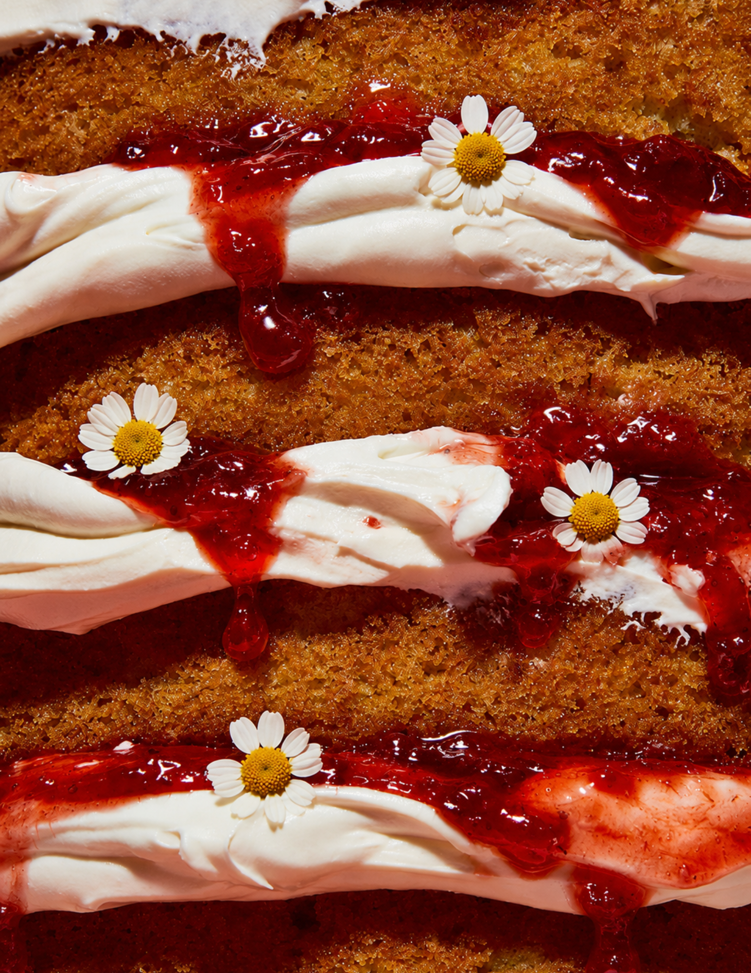 Close-up of layered cake with white cream and red berry sauce, garnished with small white flowers. The rich textures convey indulgence.