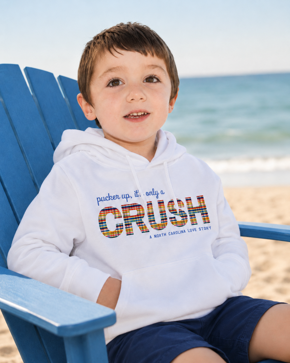 young boy in white hoodie on the beach in a chair