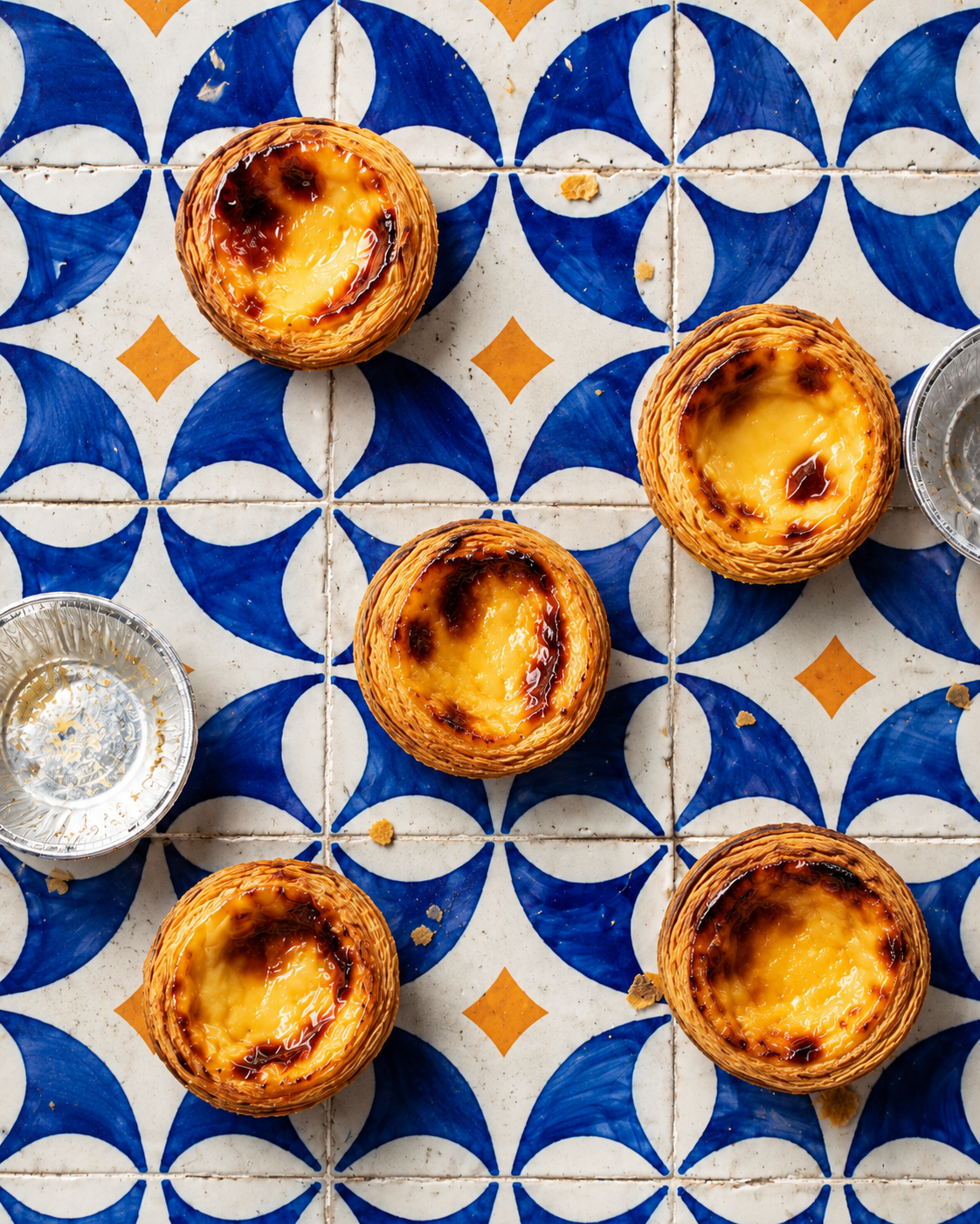 Pastel de nata custard tarts on a blue and white geometric tile background, creating a vibrant, inviting, and delicious visual layout.