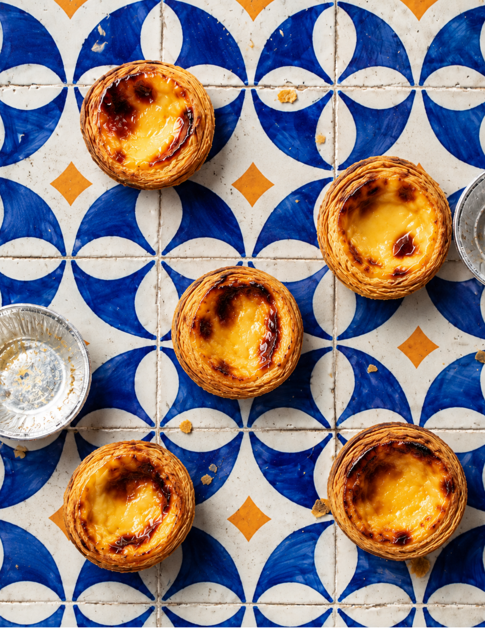 Pastel de nata custard tarts on a blue and white geometric tile background, creating a vibrant, inviting, and delicious visual layout.