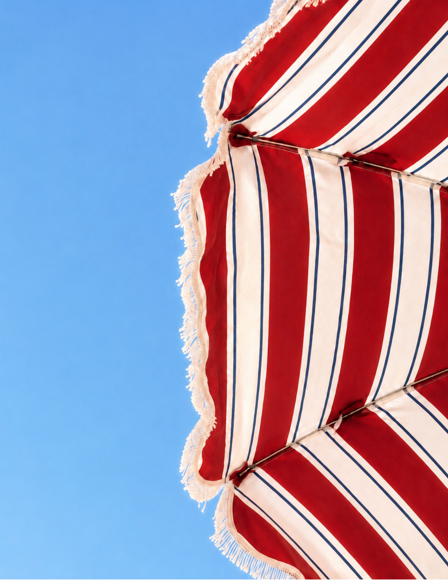 Red and white striped umbrella with fringe against a clear blue sky, creating a vibrant and sunny summer atmosphere.