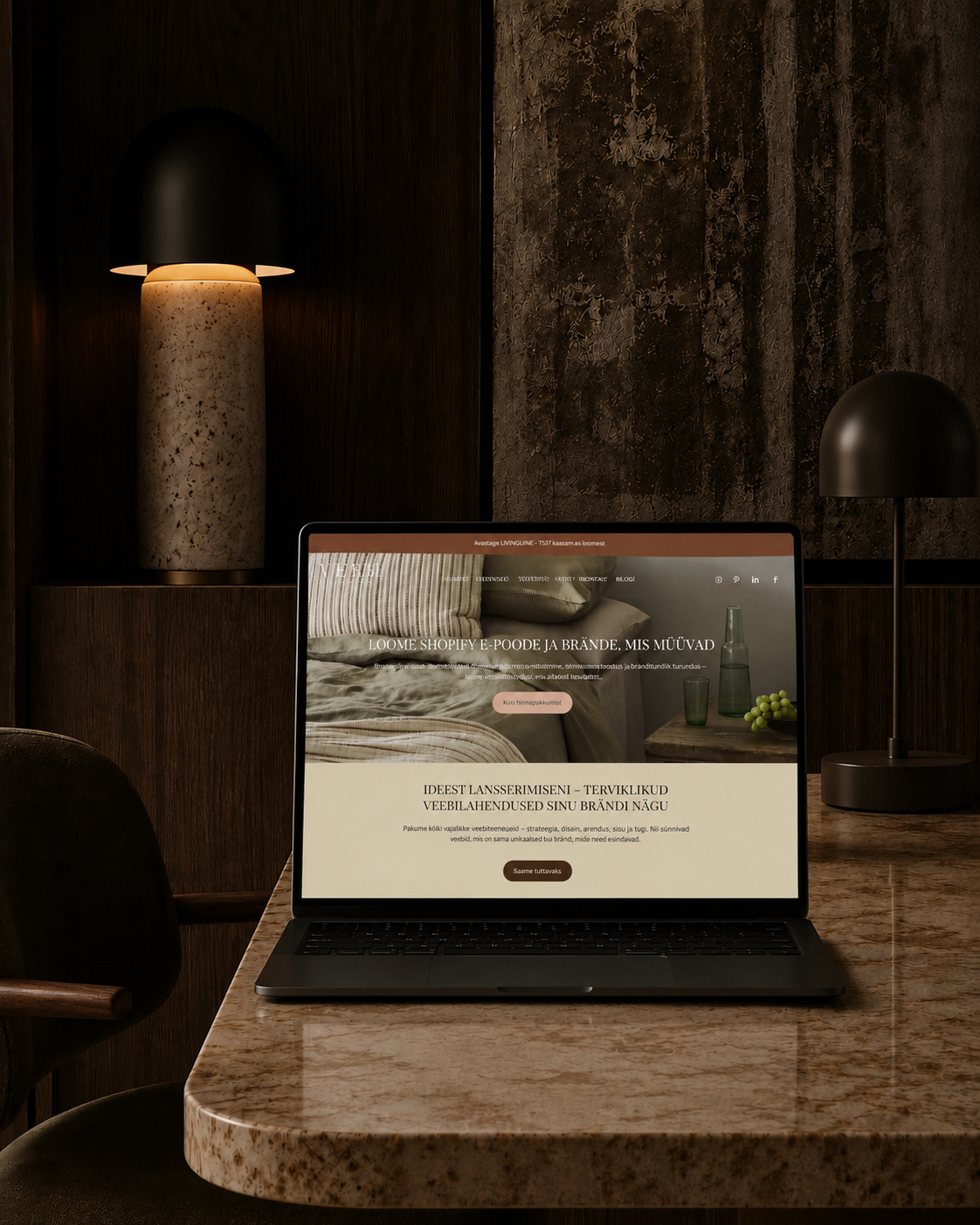 A laptop on a marble table displaying a website, with dark wooden walls and two black and beige lamps in the background.