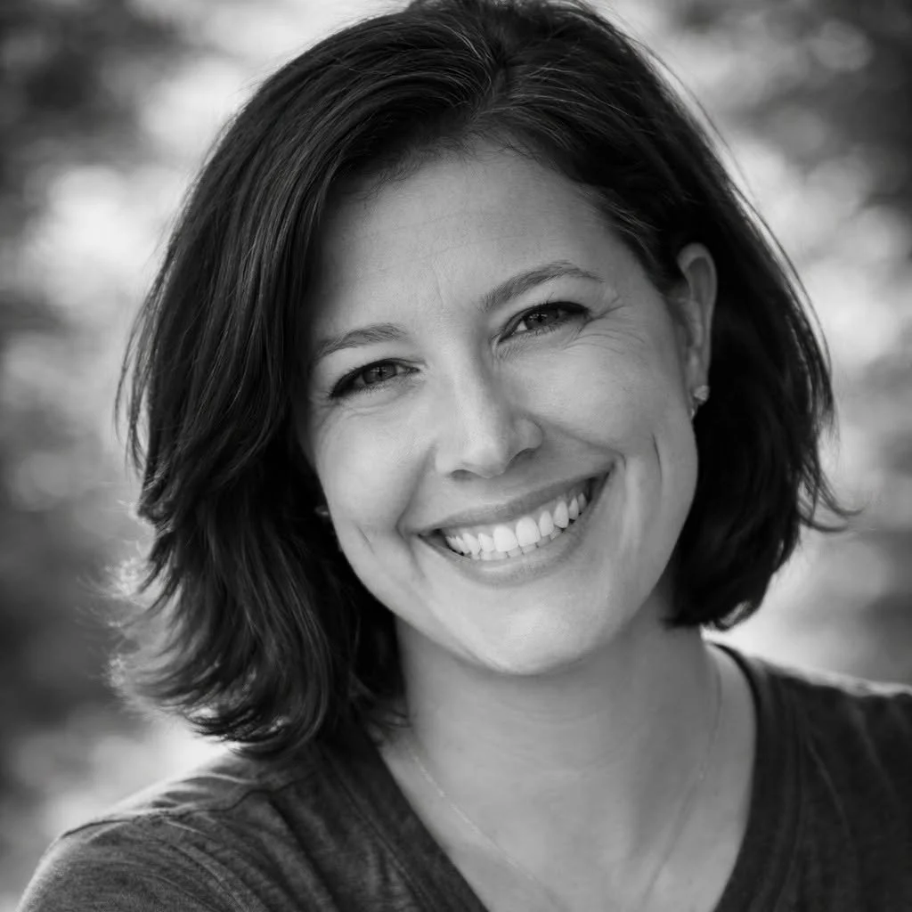 Black and white portrait of a smiling woman with shoulder-length dark hair, wearing a dark top and small earrings.