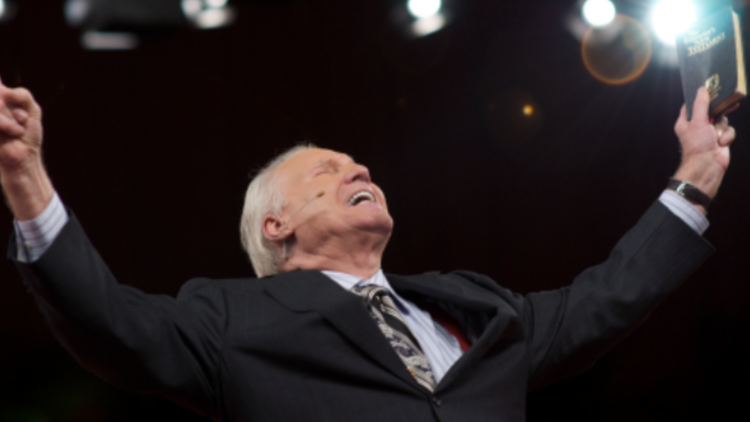 Jimmy Swaggart with hands raised in the air and holding a bible.