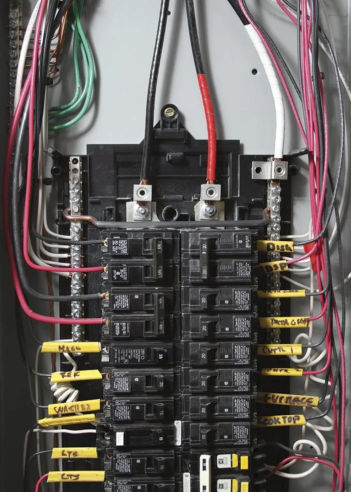 Electrical panel with various labeled circuit breakers and colored wires.