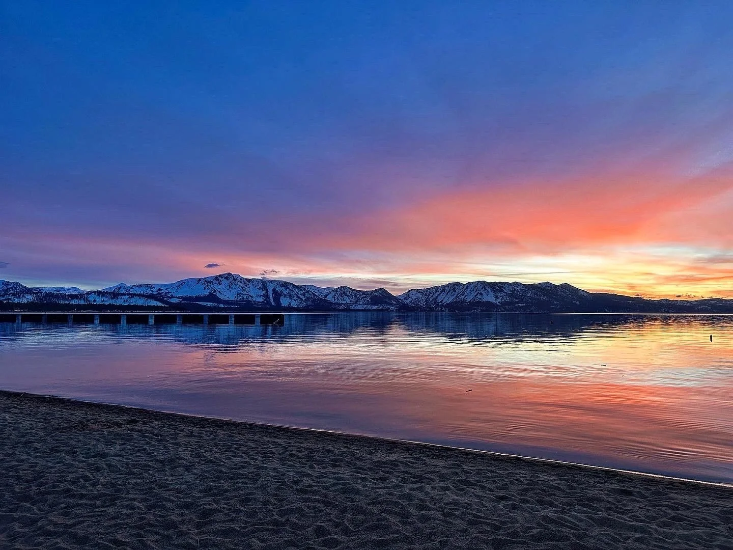 Mountains reflected in calm lake during a colorful sunset with pink, purple, and orange hues.