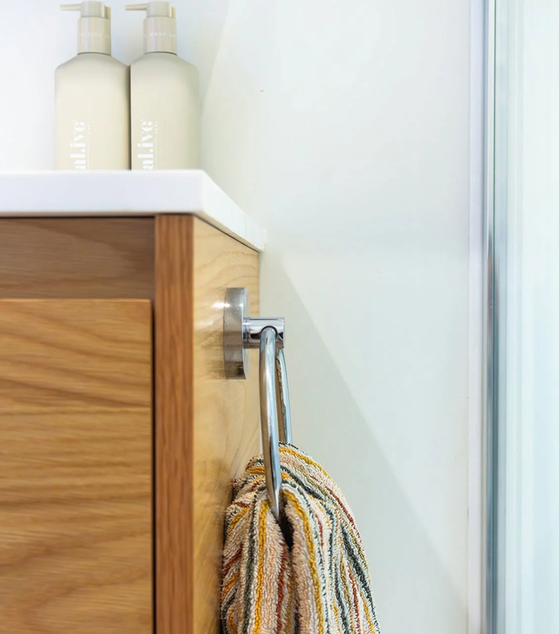 Close-up of a bathroom or vanity cabinet with a towel hanging from a chrome towel holder, and two bottles on the countertop.
