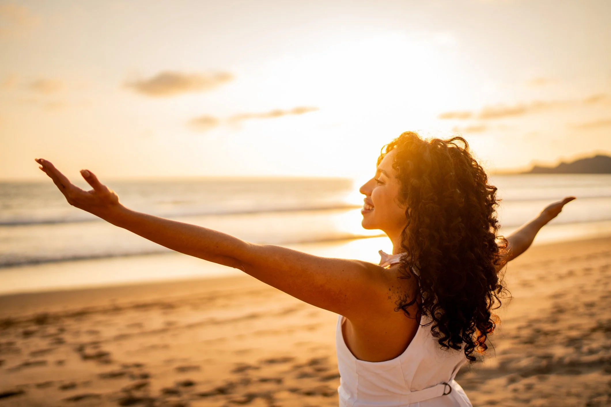 A woman smiling with her arms outstretched facing the ocean at sunset, experiencing radical cortisol reduction and emotional freedom at a luxury menopause wellness retreat in Mexico with The Menopause Strategist.