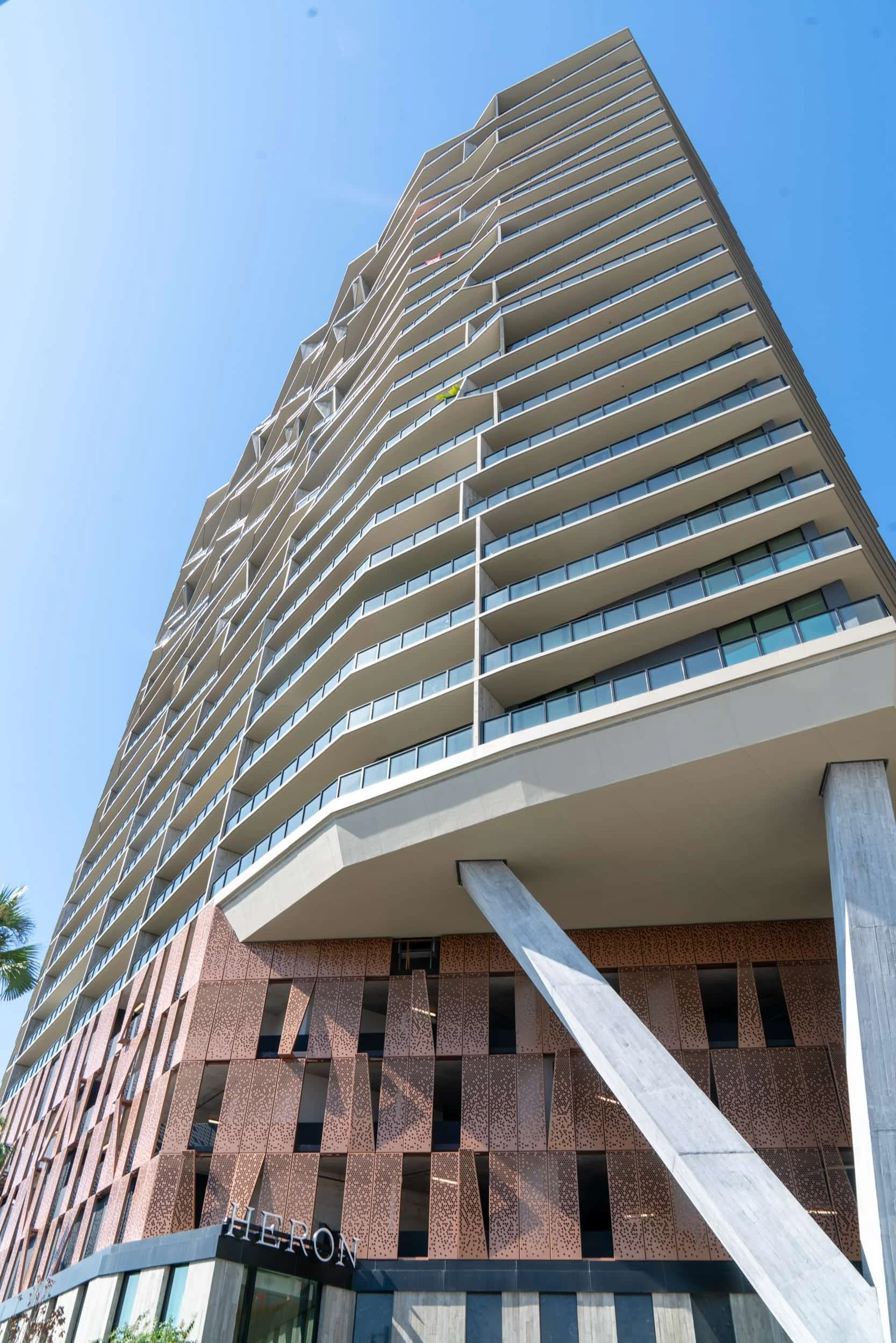 A modern skyscraper with curved balconies and glass railings, featuring the word 'HILTON' at the base, set against a clear blue sky.