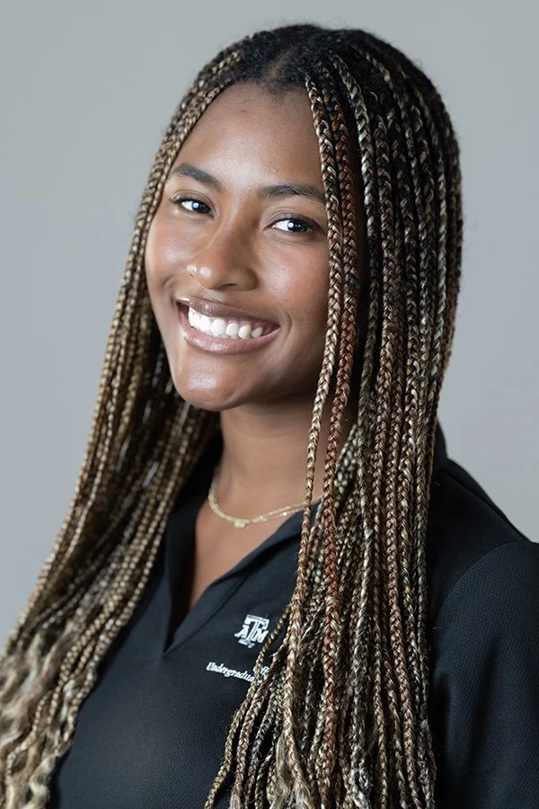 Young woman with long, braided hair smiling at the camera wearing a black shirt.
