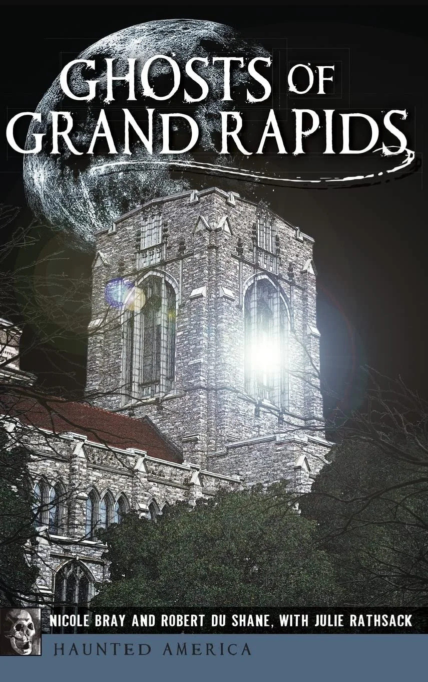 Book cover titled 'Ghosts of Grand Rapids' shows a large, old stone church with Gothic architecture, backlit with bright light, under a full moon with a swoosh line, dark sky, and some trees in the foreground.