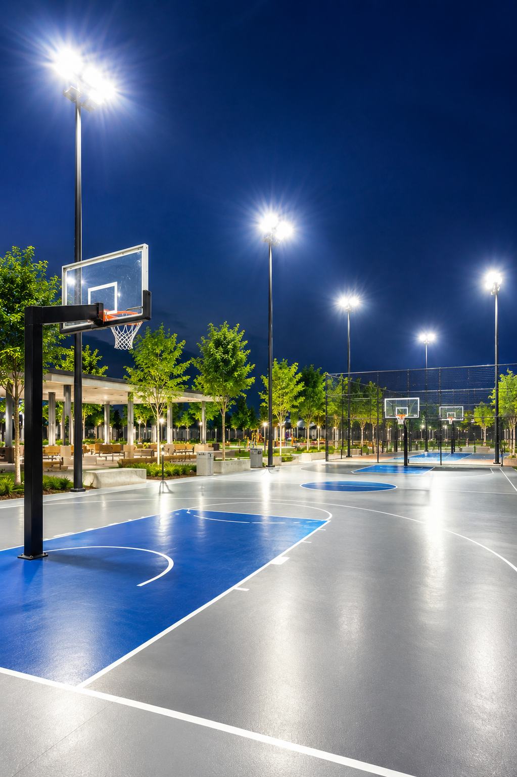 Cancha de baloncesto iluminada en la noche, rodeada de árboles y farolas en un parque