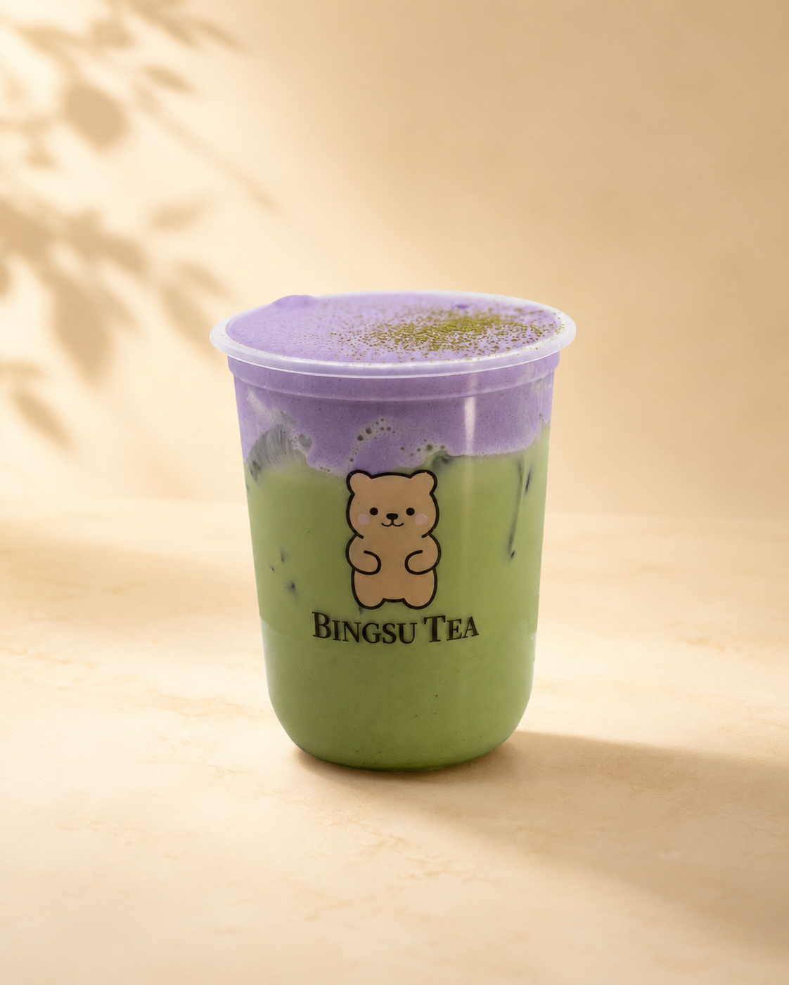 A plastic cup filled with a green and purple layered drink, labeled 'Bingsu Tea' with a bear logo on the front.