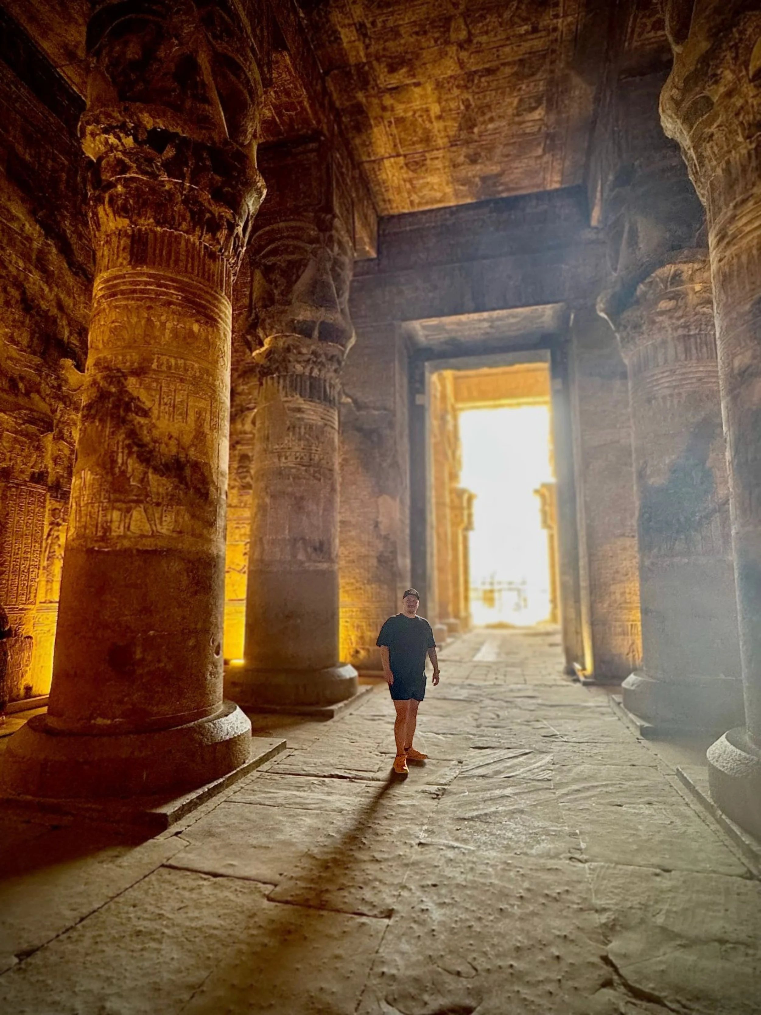 A person walking inside an ancient Egyptian temple with large carved stone columns, illuminated by sunlight coming through the doorway.