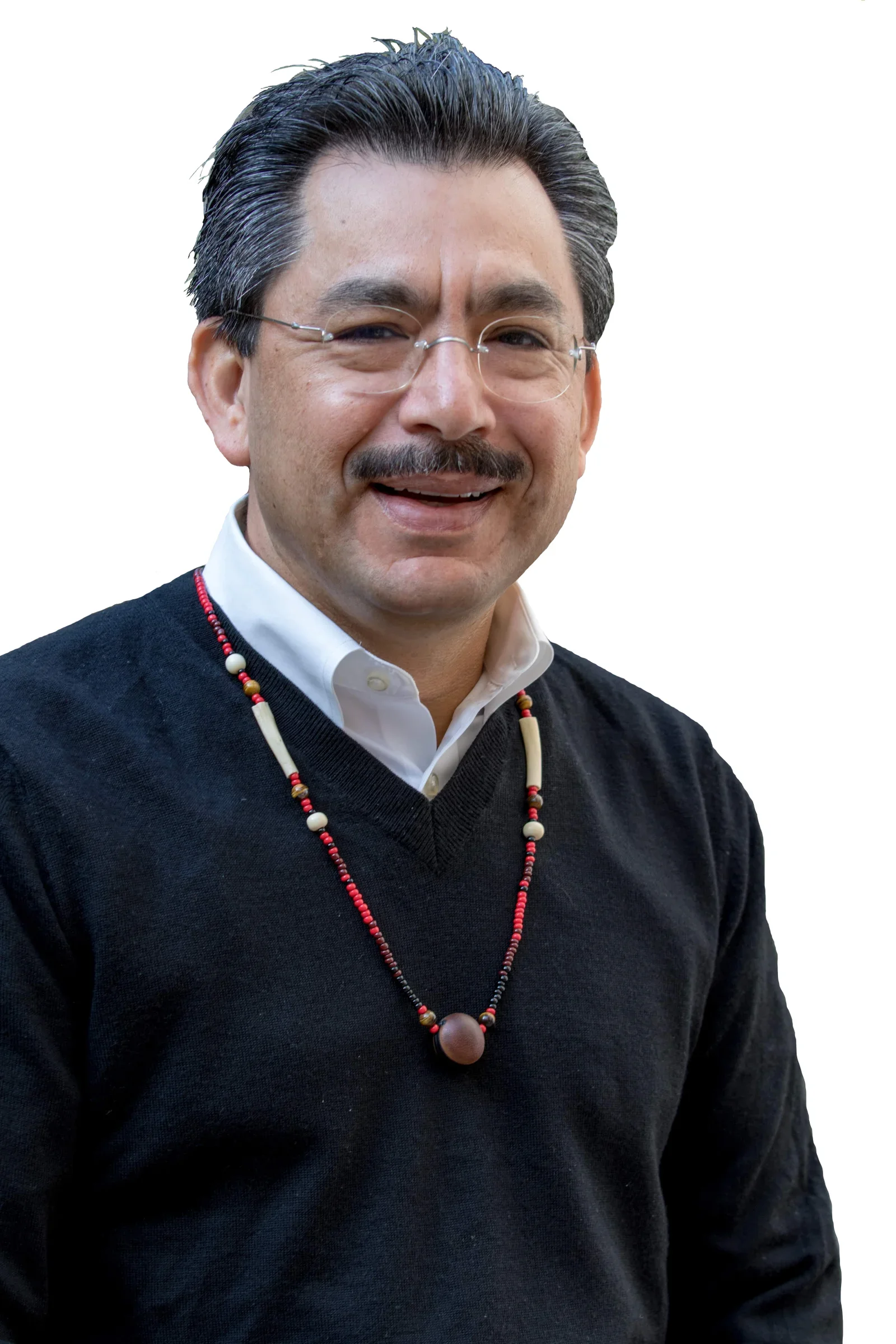 A middle-aged man with glasses, a mustache, and black hair with gray streaks, smiling, wearing a white collared shirt, a black sweater, and a beaded necklace against a plain white background.