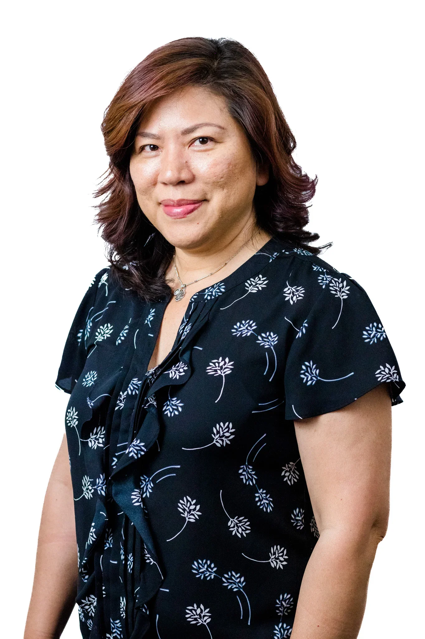 A woman with shoulder-length brown hair wearing a navy blue dress with white floral patterns and a necklace, smiling at the camera against a white background.