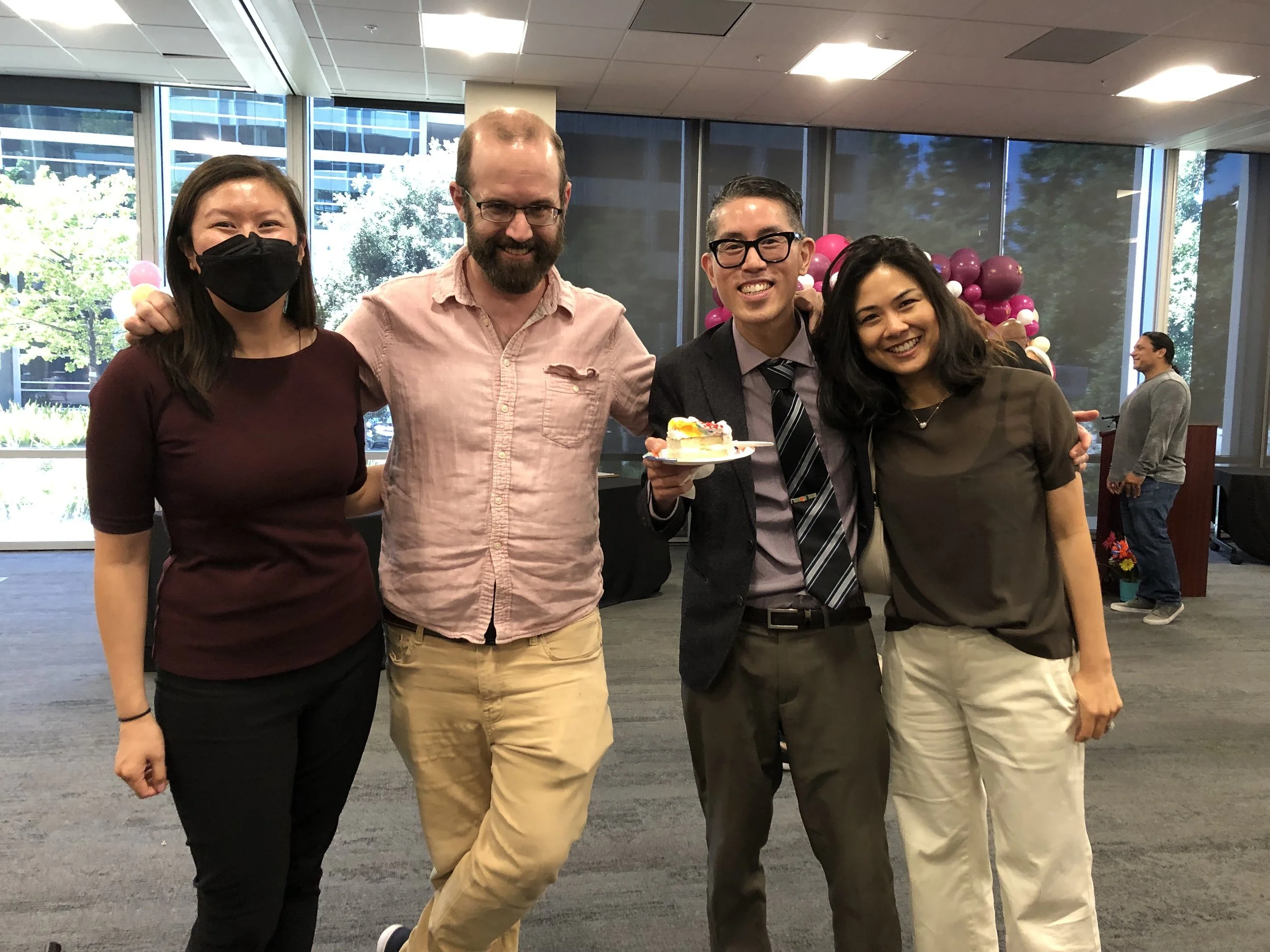 Group of four people smiling at the 13th Annual Family Reunification Day Celebration, holding a slice of cake.