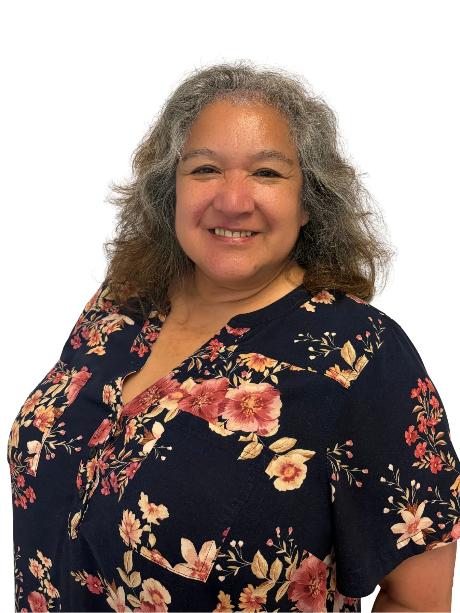 A woman with curly gray hair smiling, wearing a navy floral shirt with pink and cream flowers.