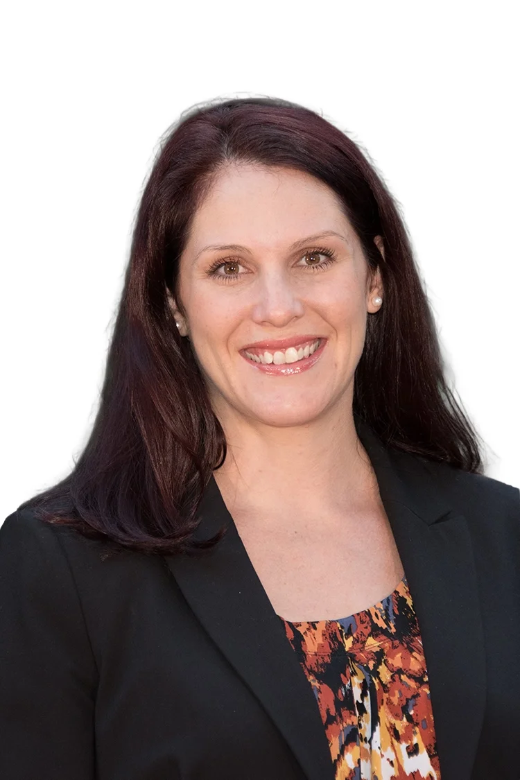A professional woman with brown hair smiling, wearing a black blazer and a colorful patterned top against a white background.
