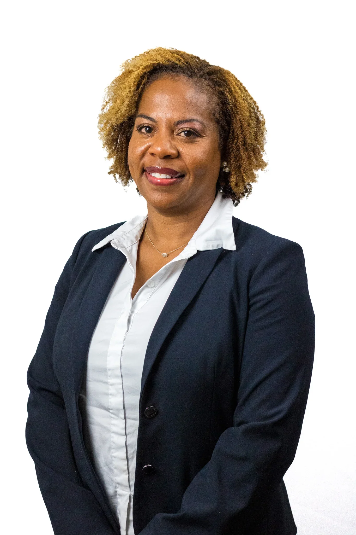 Portrait of a professional woman with curly blonde hair, wearing a dark blazer, white shirt, pearl earrings, and a necklace, against a plain white background.