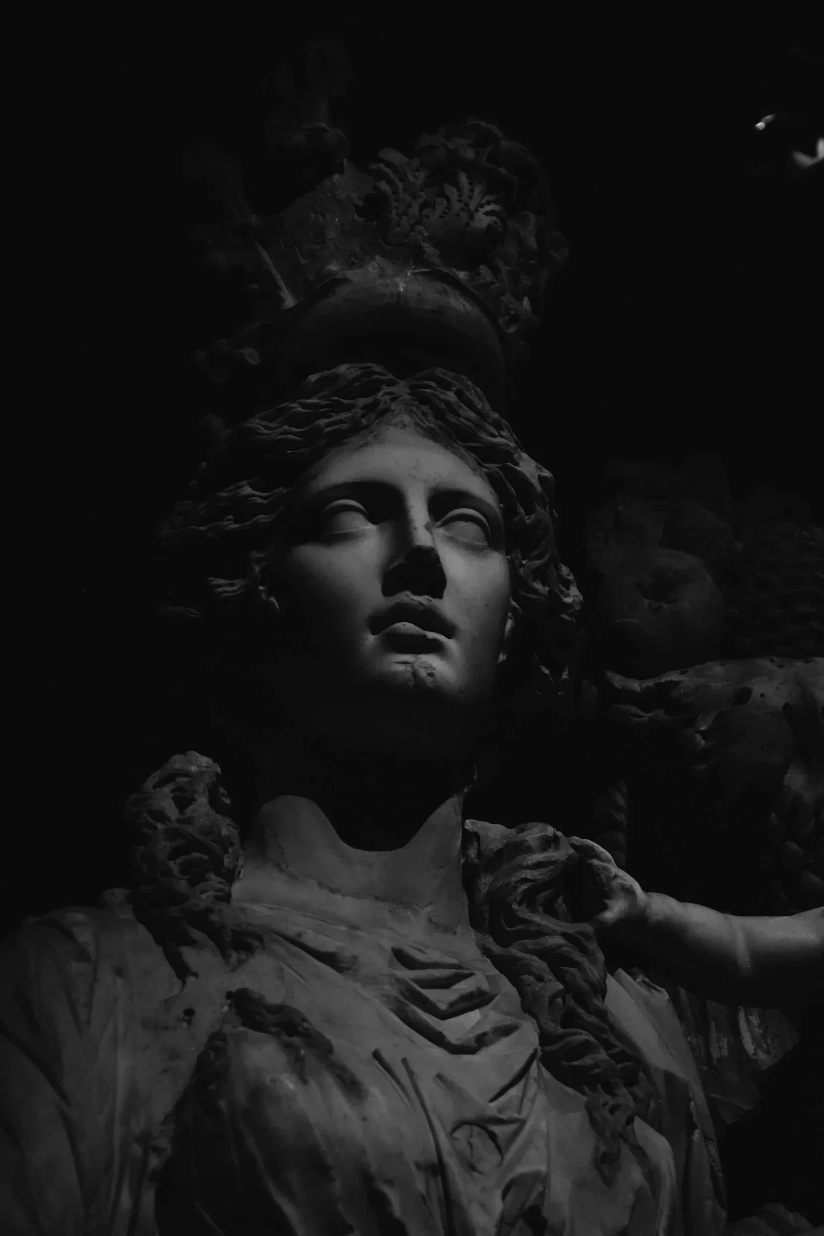 Black and white photo of a large, detailed sculpture of a woman with wavy hair, surrounded by decorative elements, with a dark background.