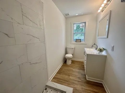 Small bathroom with white walls, a window, a toilet, a white vanity with a sink, and a mirror.
