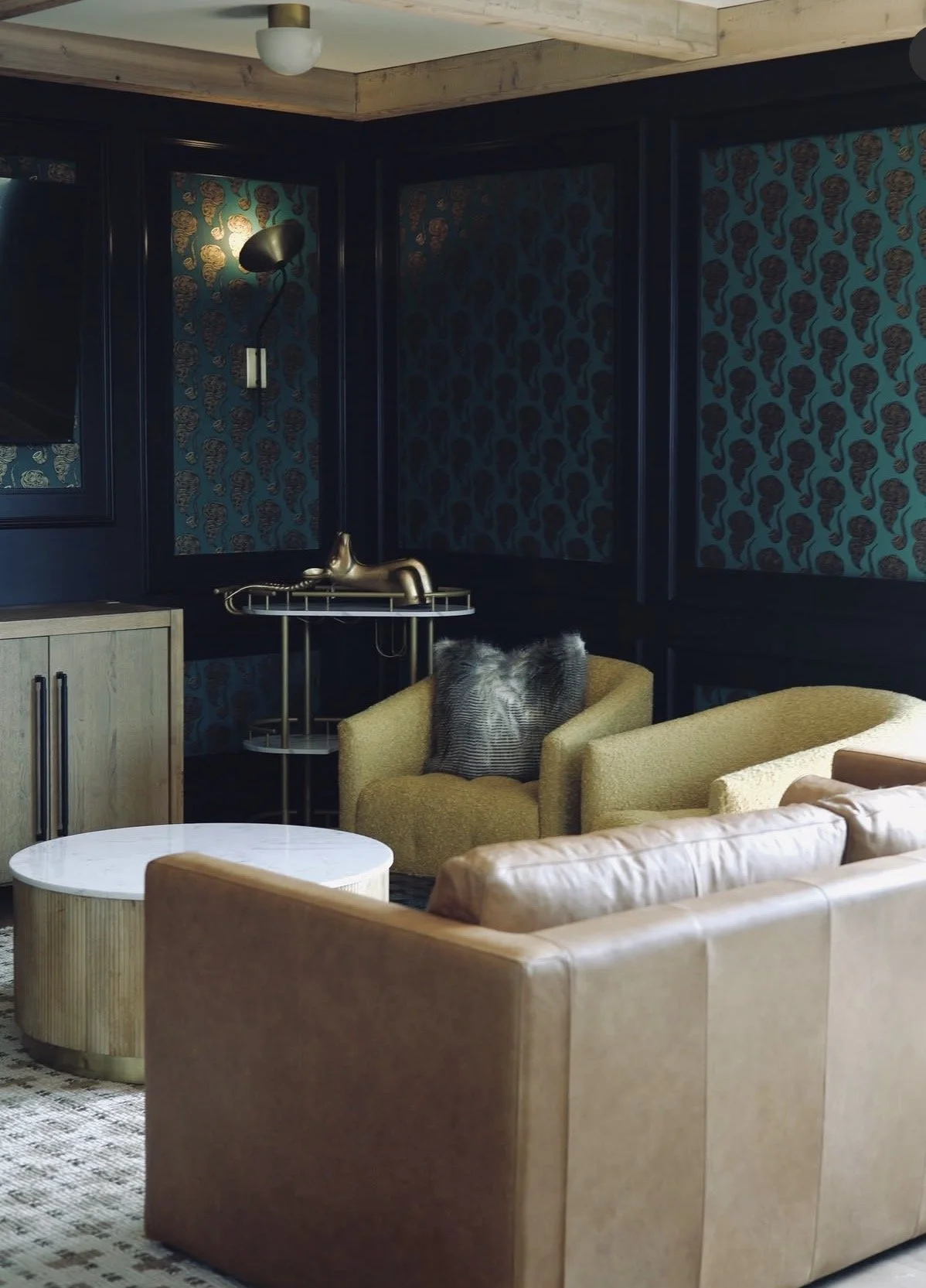 Living room with beige and yellow chairs, a white coffee table, a black patterned wall with a black wall lamp, a wooden cabinet, and decorative wallpaper with a tiger stripe pattern.
